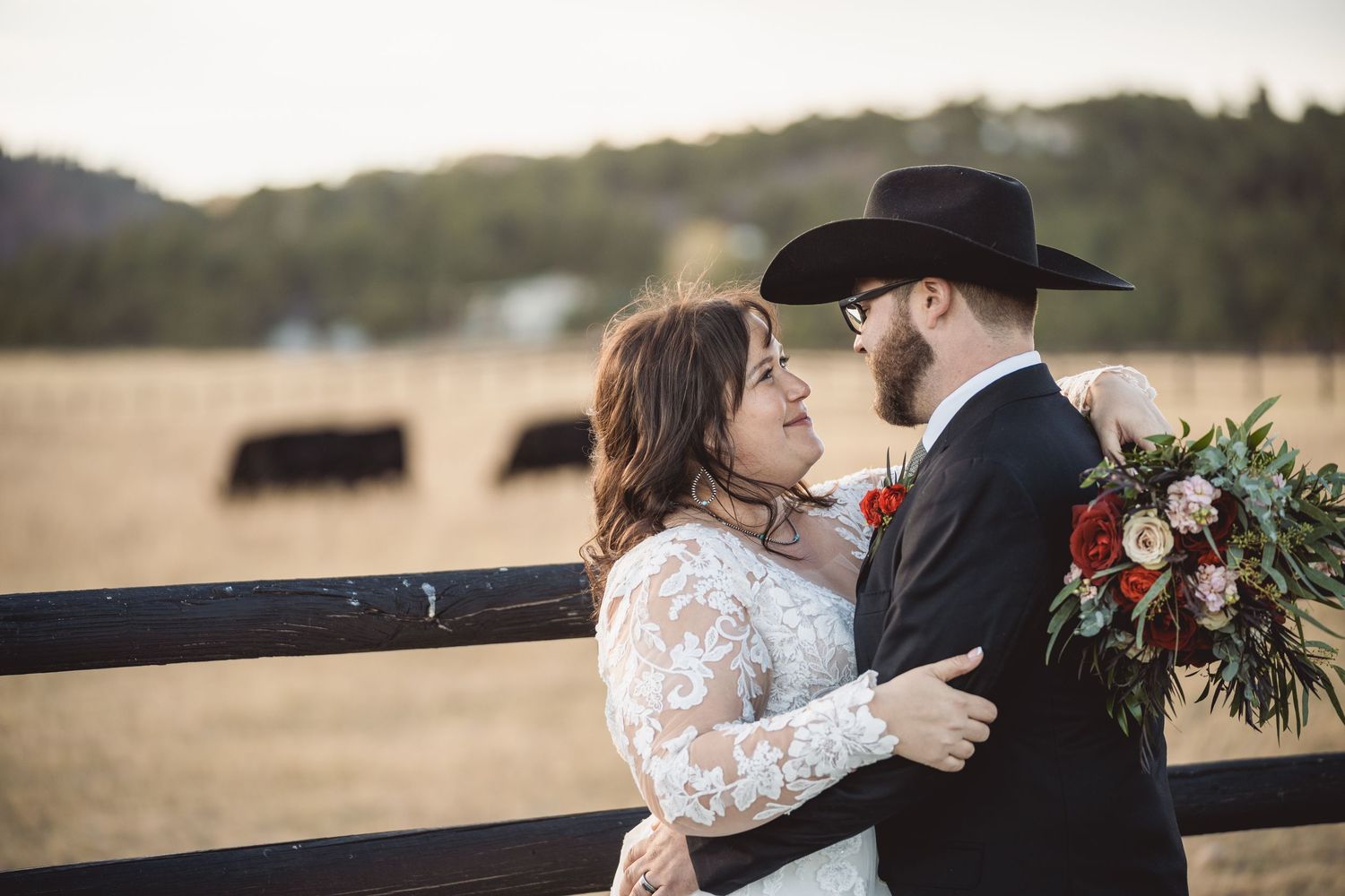 Couple embracing by rustic wooden fence at golden hour.