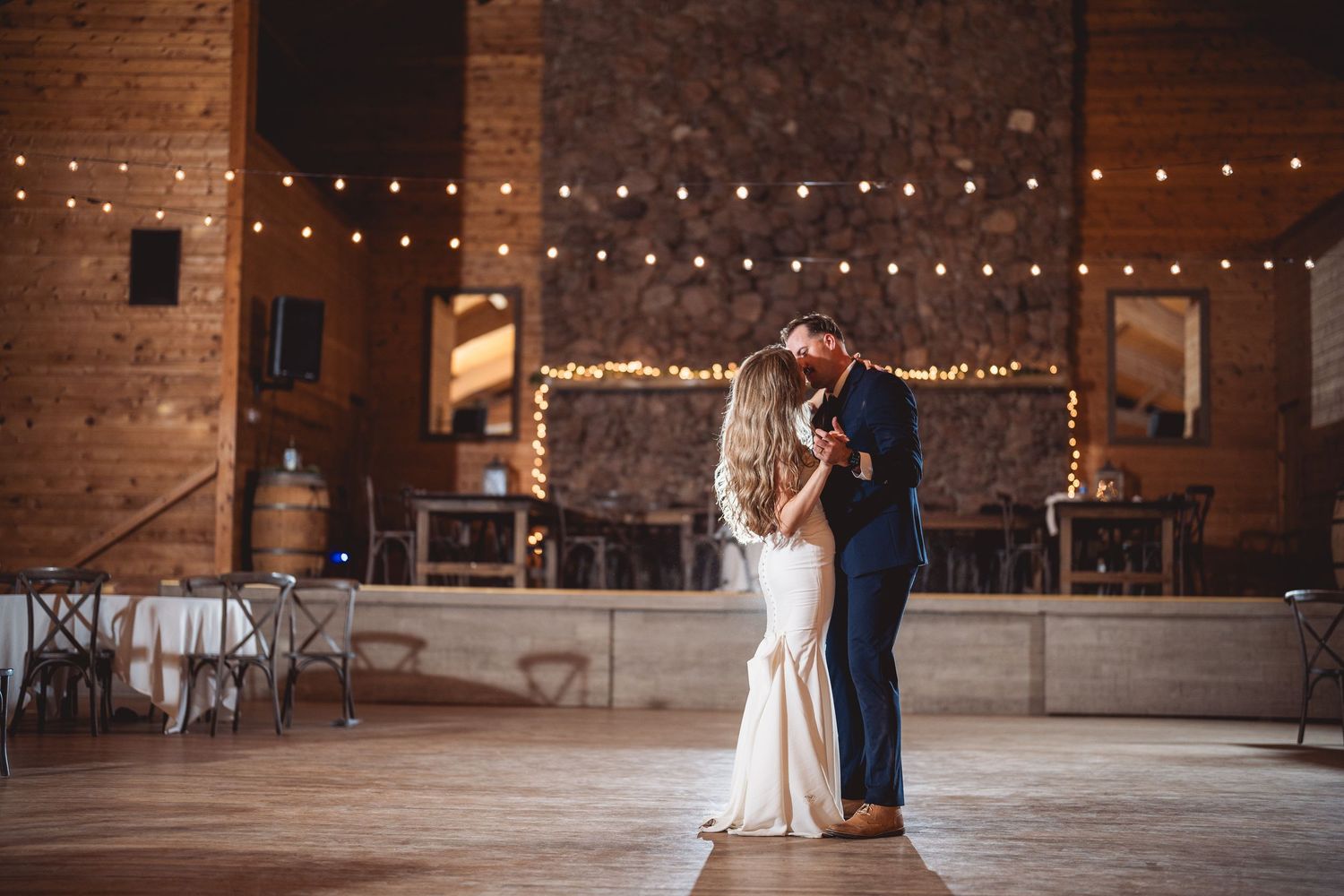 Bride and groom share an intimate first dance in a warmly lit barn with string lights.