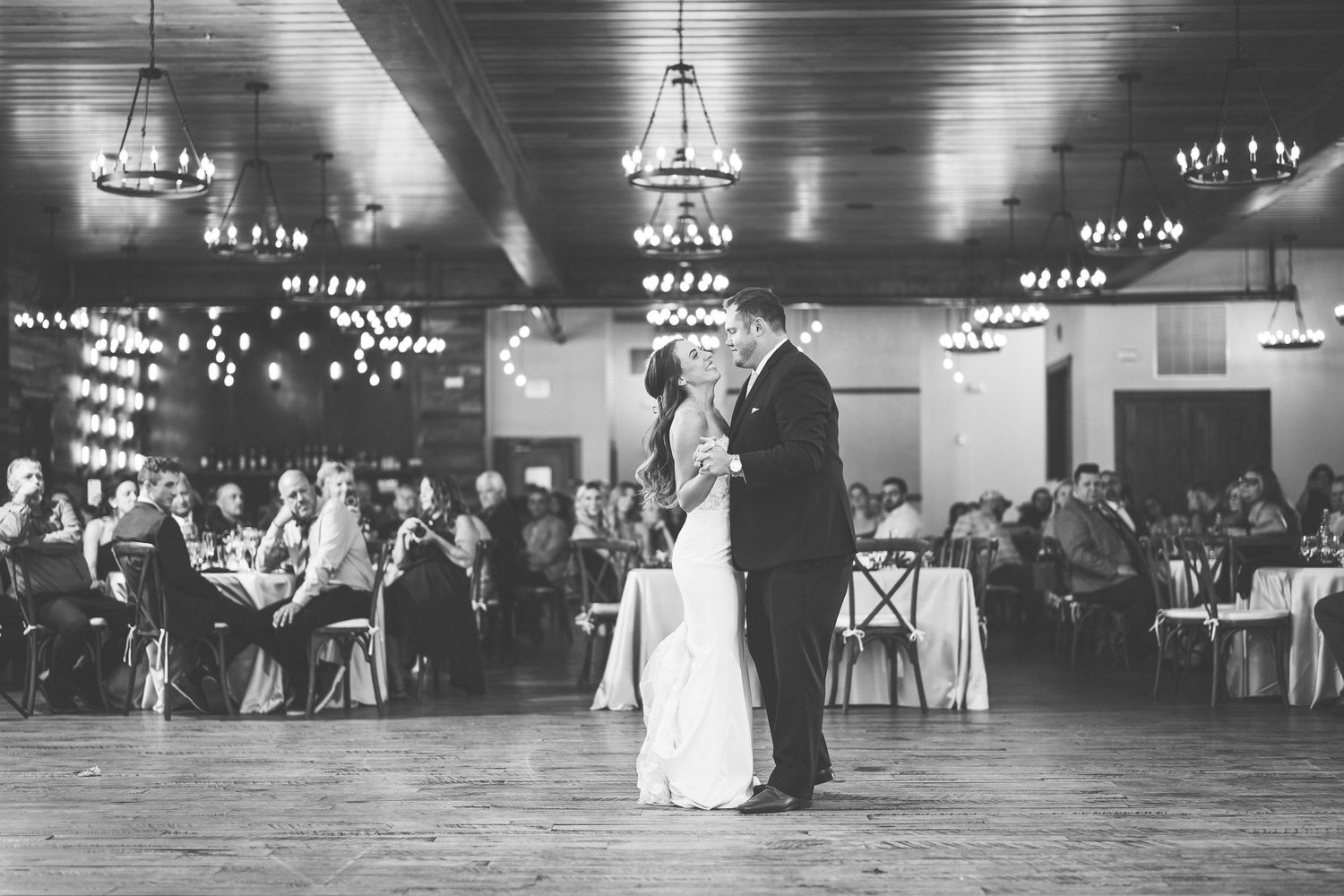 Black and white photo of a couple sharing their first dance at a wedding reception in an elegant ballroom.