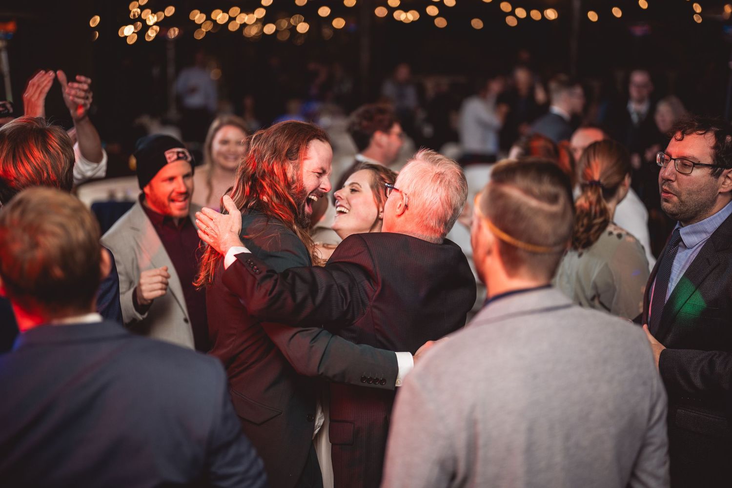Wedding guests dance and celebrate on a dimly lit dance floor during evening reception.