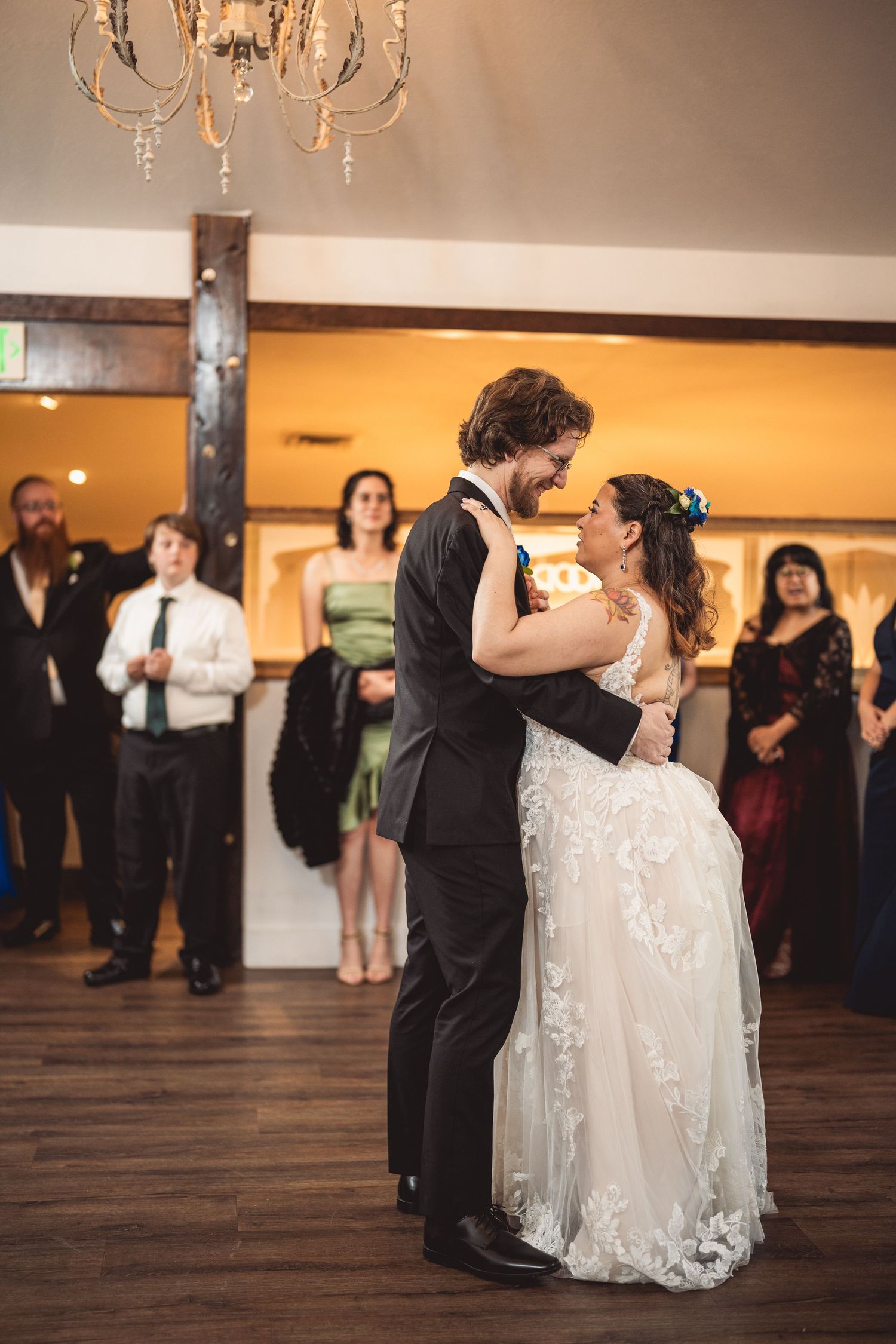A wedding couple's first dance under chandeliers in a reception hall with hardwood floors.