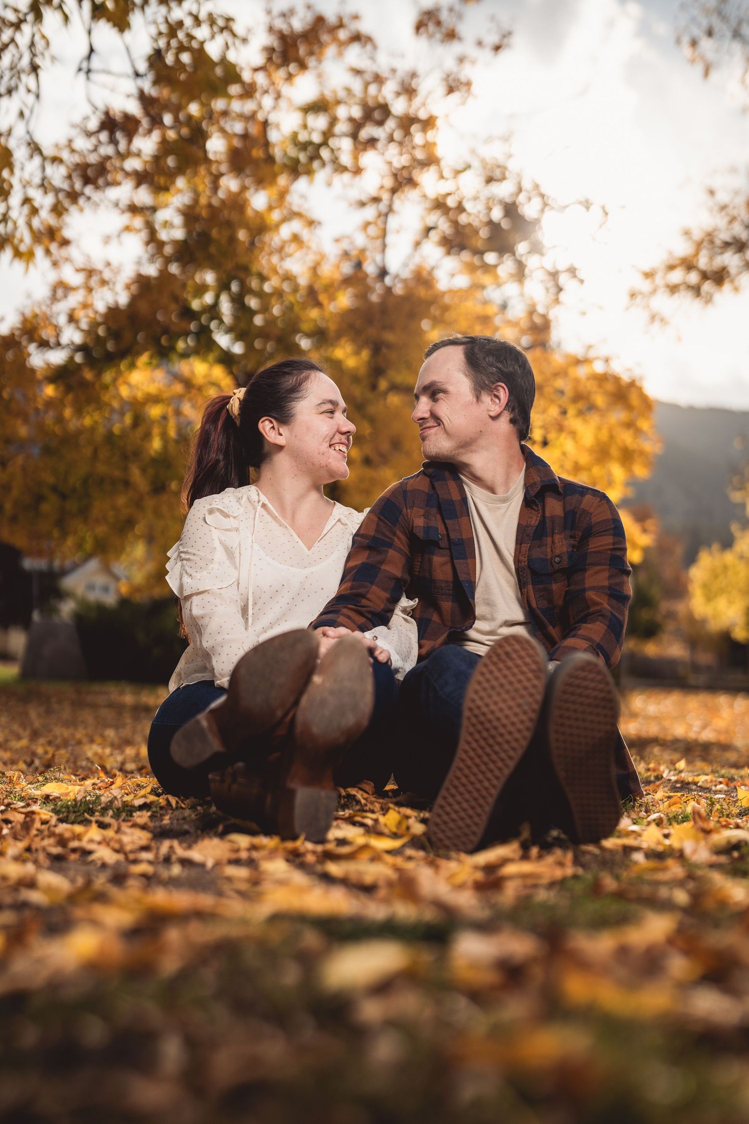 Couple laughing together while lying on fallen autumn leaves at sunset.
