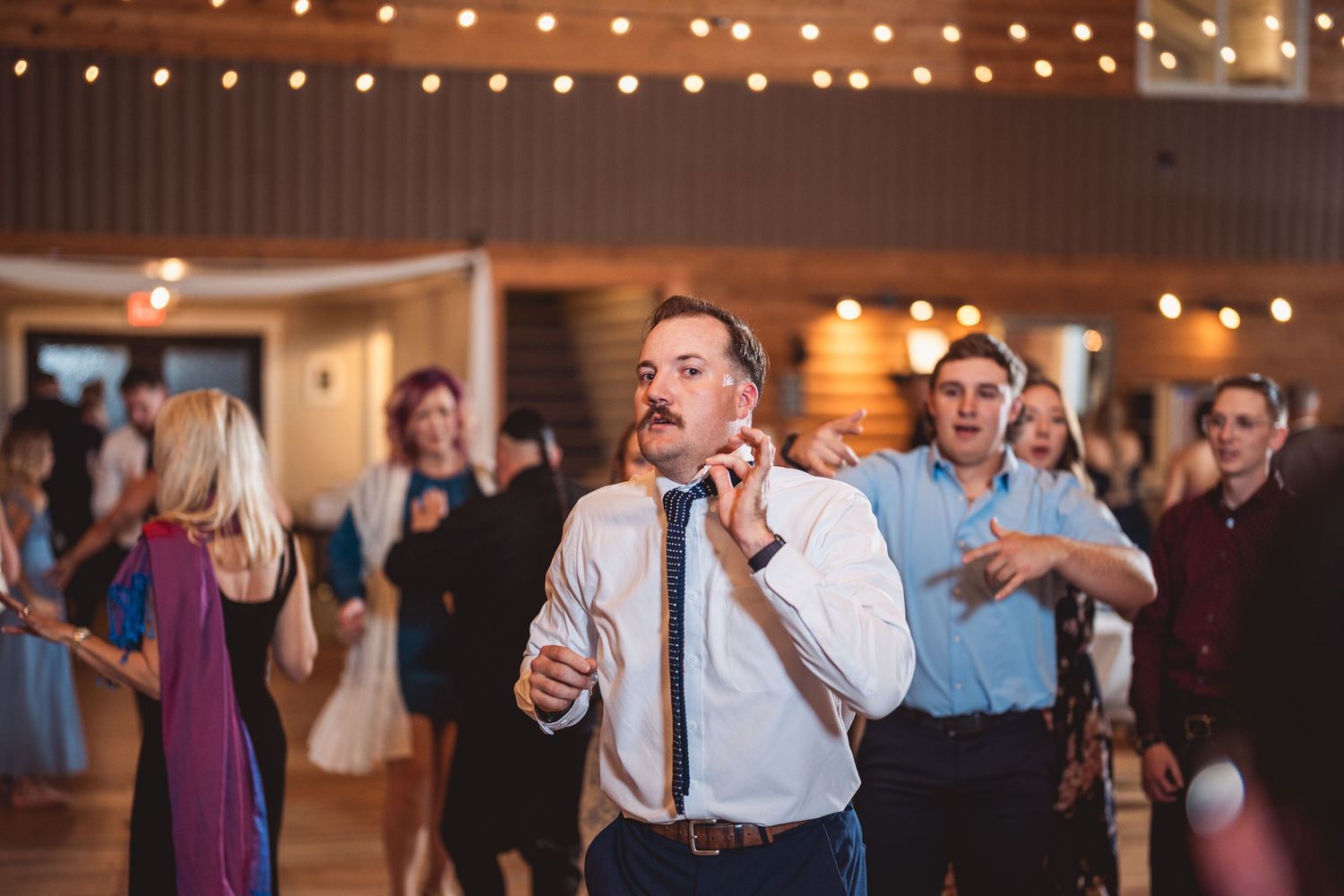 Wedding reception dance floor filled with guests celebrating under warm string lights.