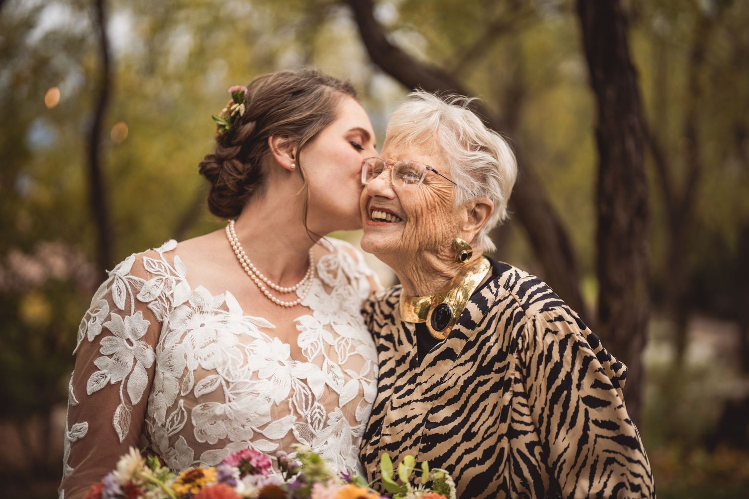Sweet moment shared between women at outdoor wedding celebration surrounded by autumn trees.