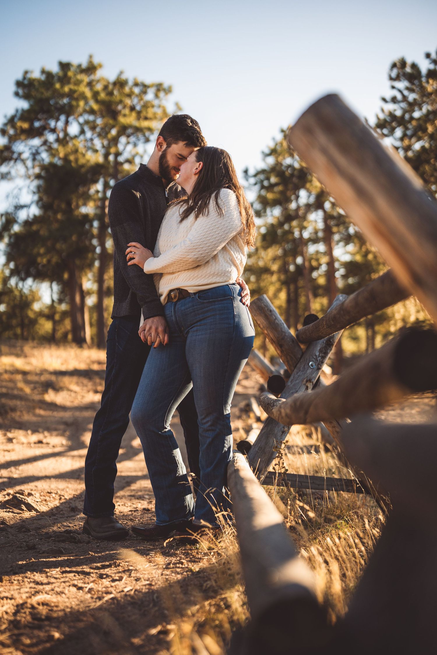 A couple shares a romantic moment among pine trees during golden hour.
