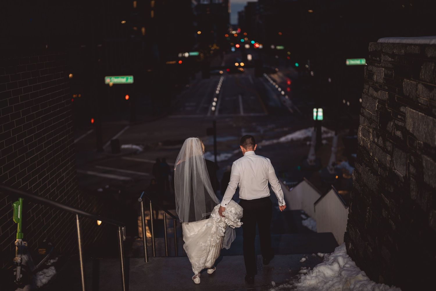 A couple walks through city streets at night after their wedding celebration.