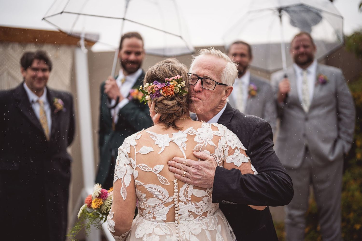 Wedding party members smile under white umbrellas during outdoor celebration.