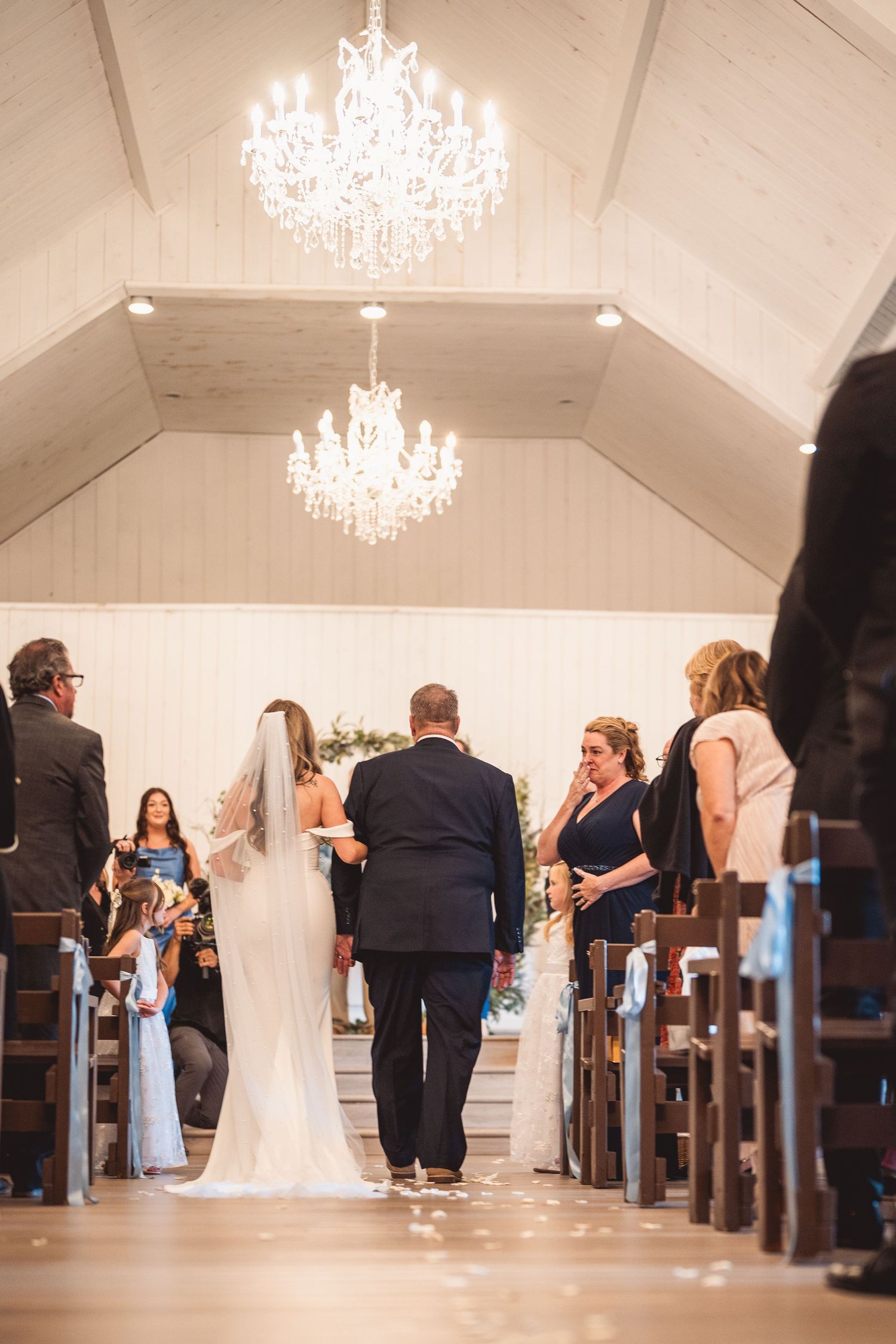 Wedding ceremony in bright chapel with crystal chandeliers and wooden pews.