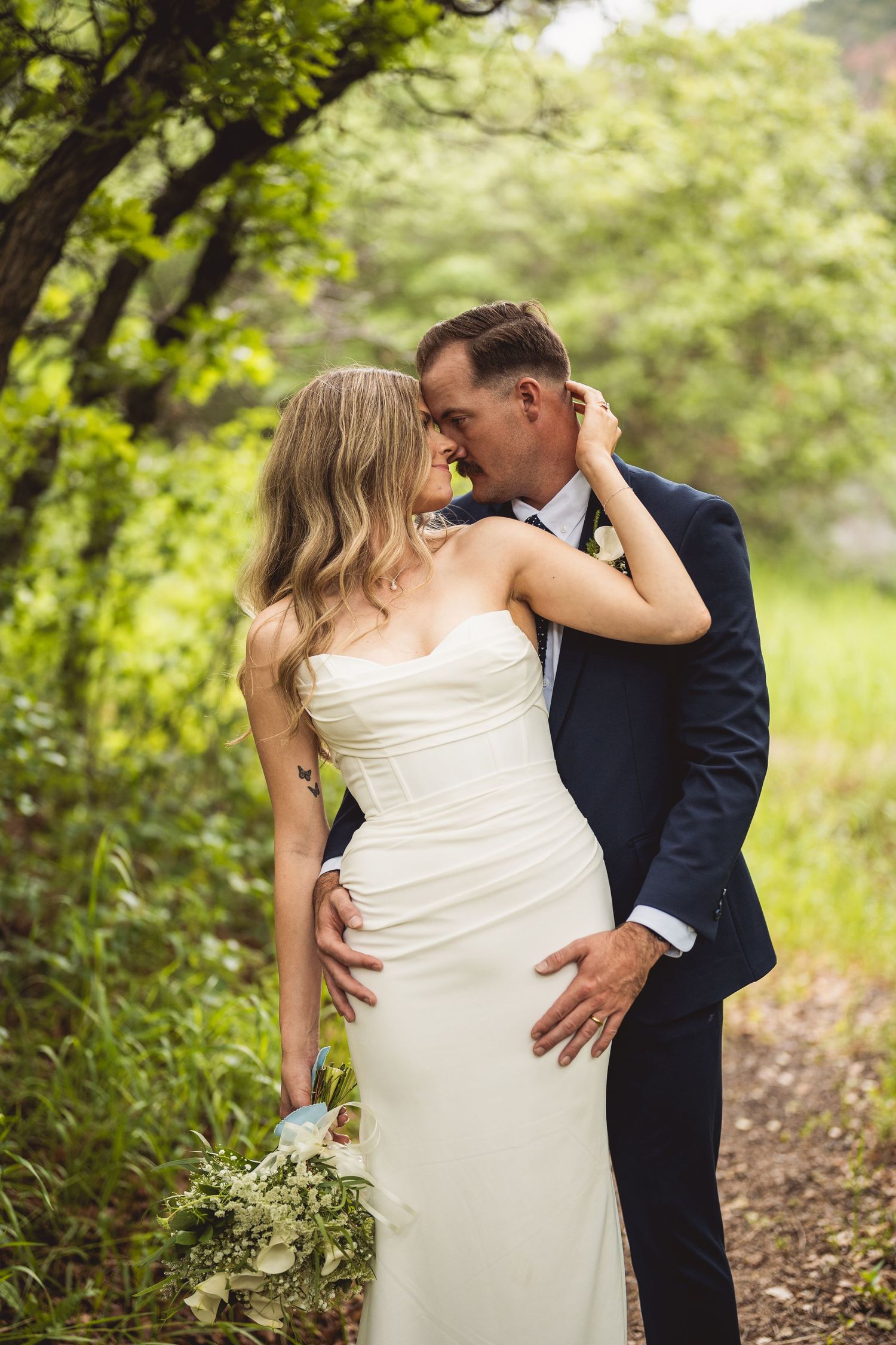 A romantic embrace between a couple in wedding attire surrounded by vibrant spring foliage.