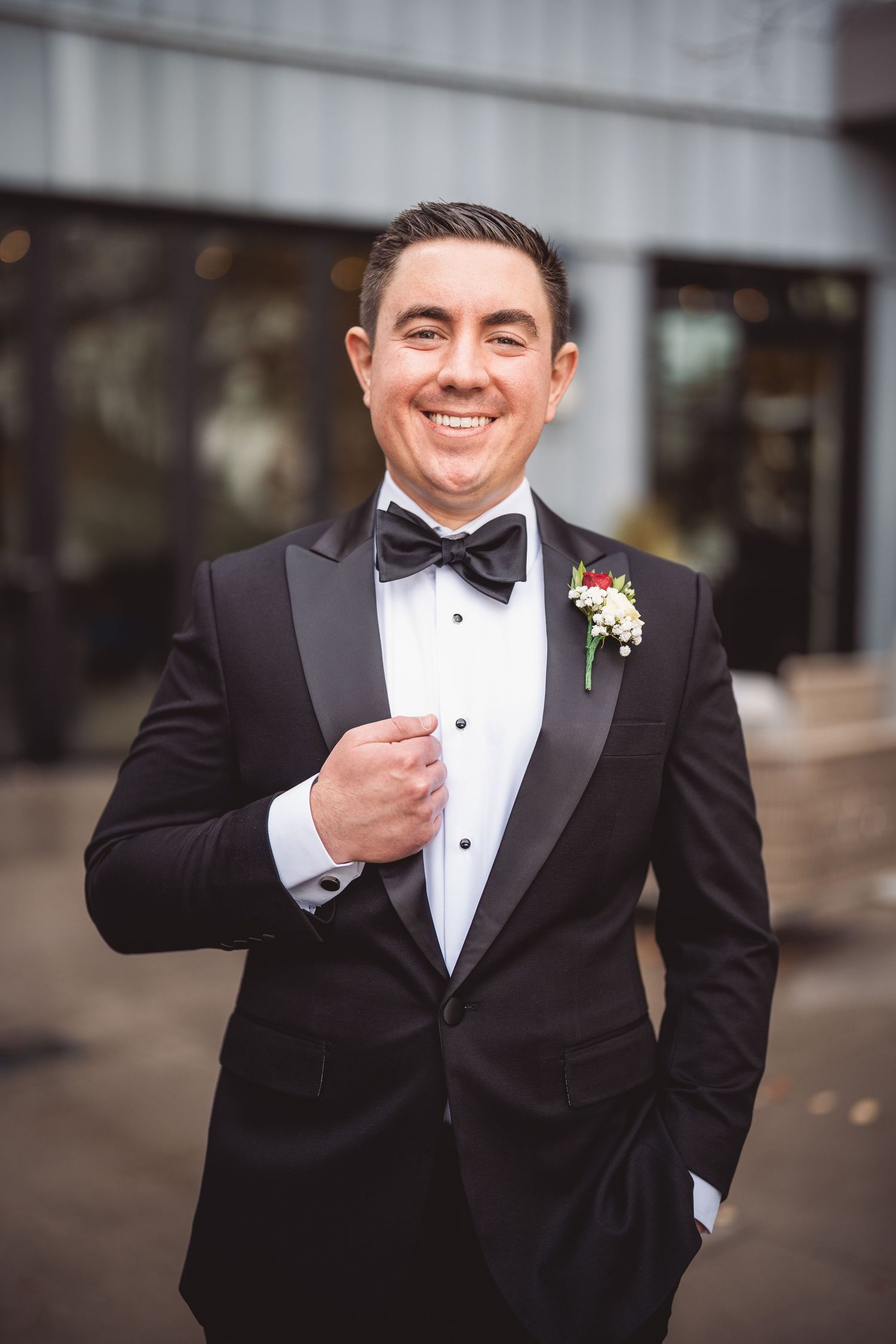 Groom adjusts his bowtie while wearing a classic black tuxedo with boutonniere.