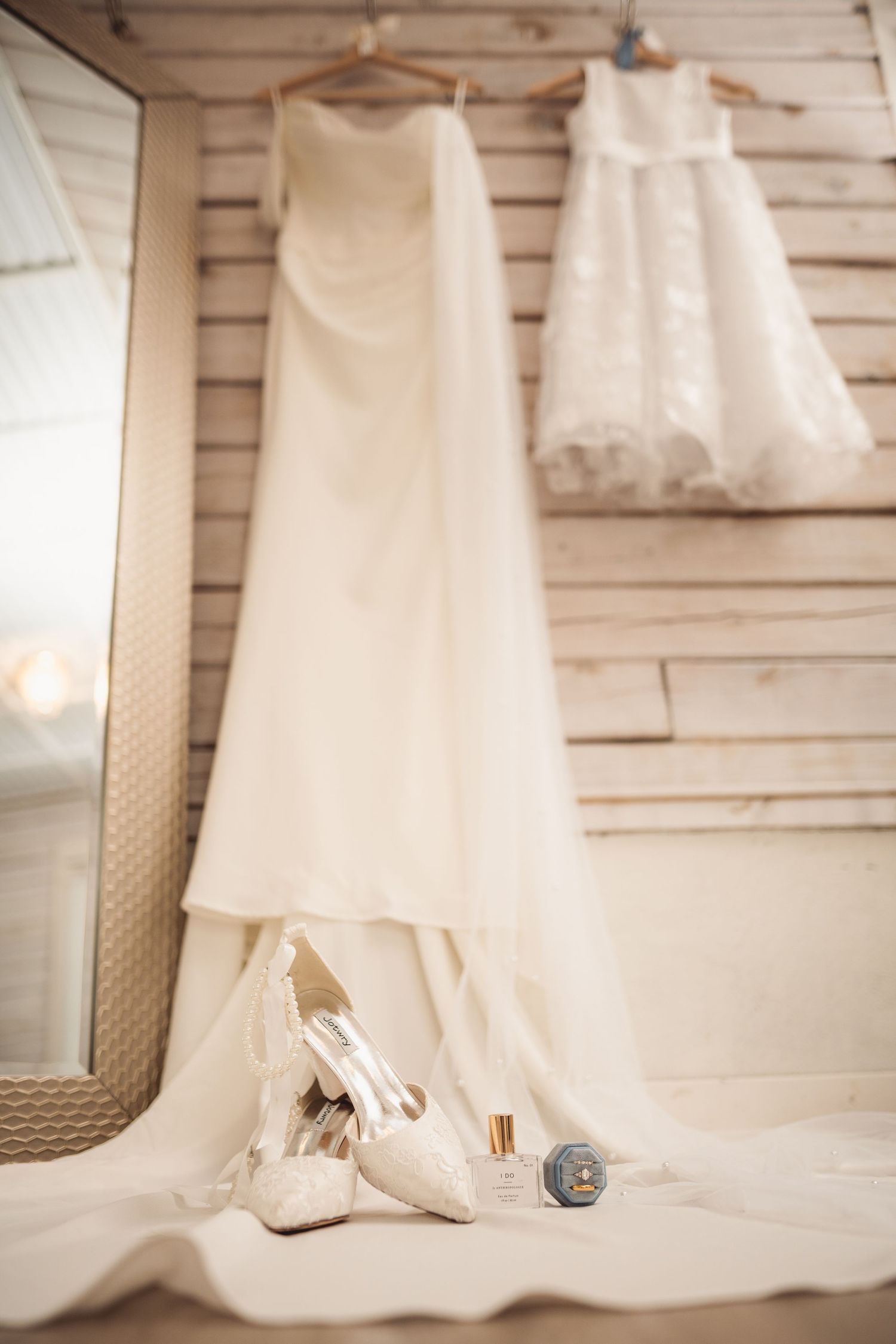 Wedding dress details and accessories photographed against white wooden wall.