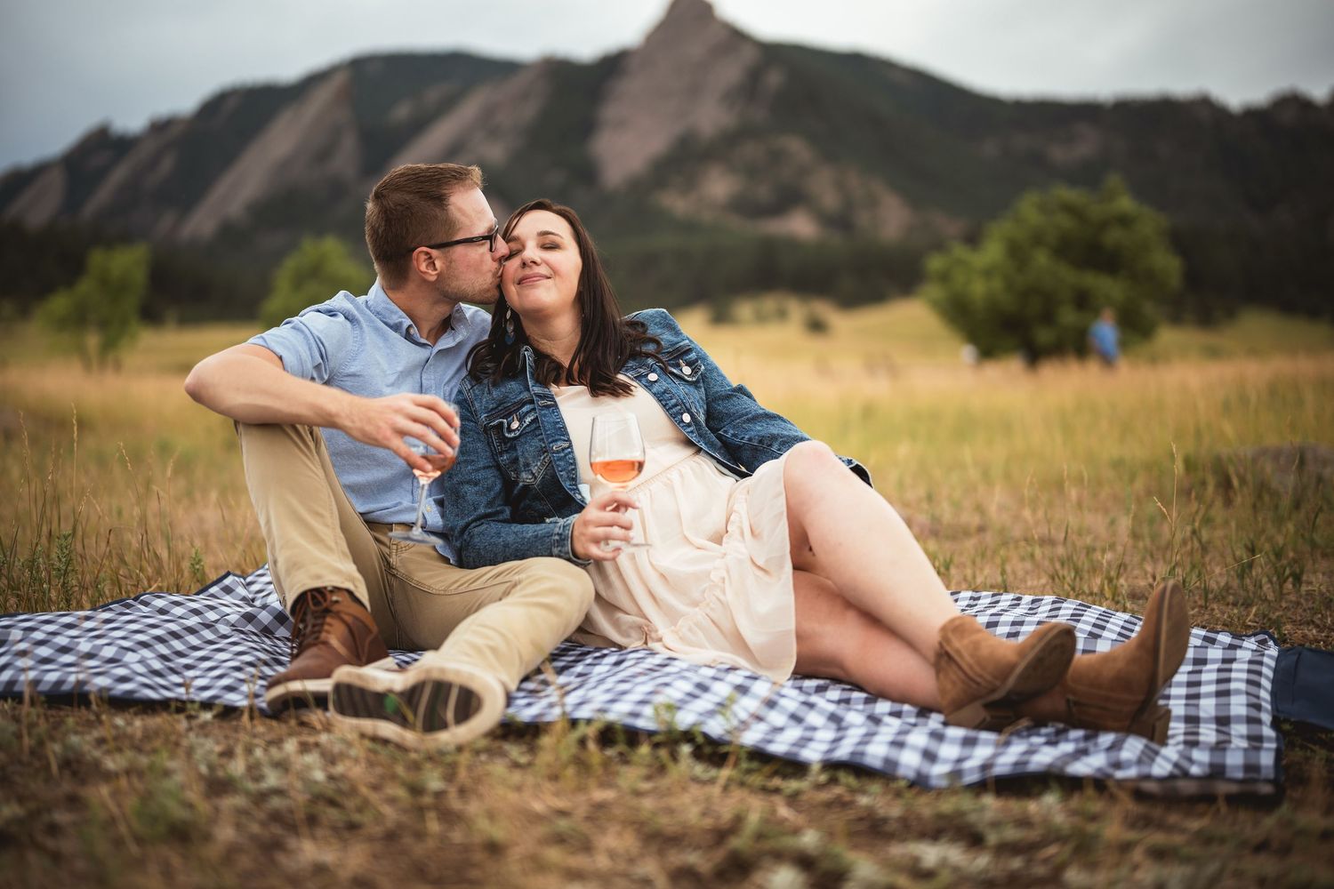 Couple sharing wine on a picnic blanket in a mountain meadow, enjoying a romantic outdoor date.