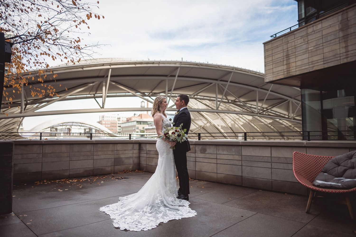 Bride and groom share a romantic moment on a rooftop terrace with an arched glass structure backdrop on their wedding day.