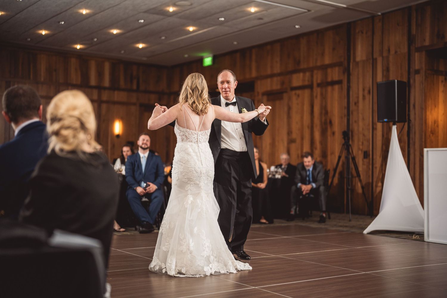 Bride and groom share their first dance in a rustic barn wedding venue with guests watching.