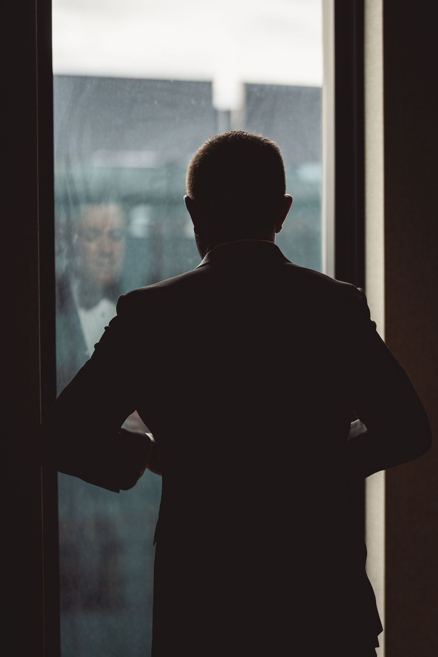 Silhouette of person in suit standing against window with hands on hips.