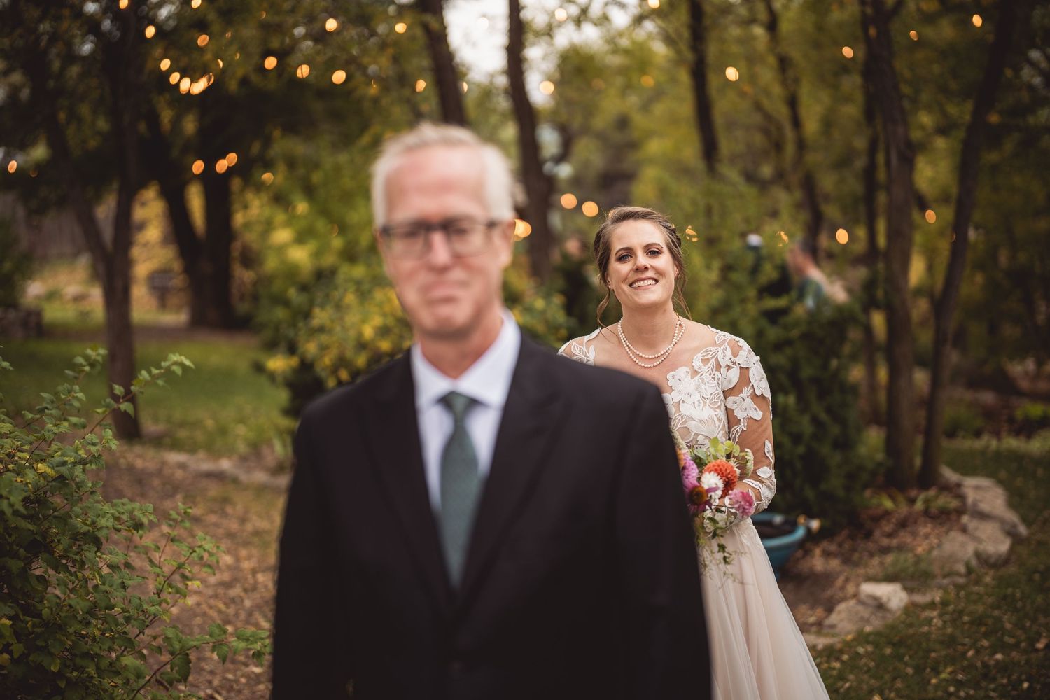 Wedding party members walking through an outdoor setting with string lights and autumn foliage.