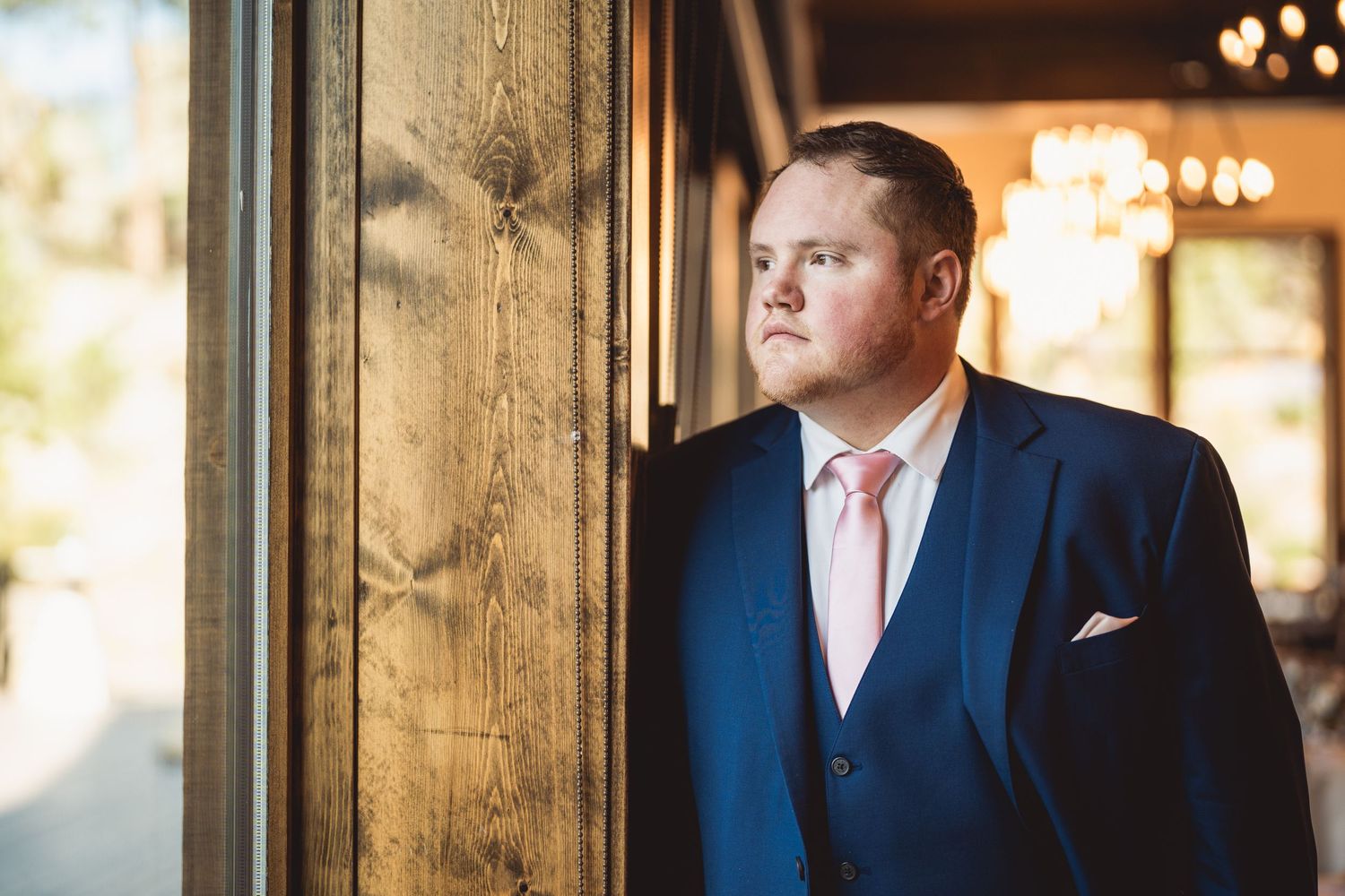 Person in navy suit standing by wooden beams in warmly lit venue.
