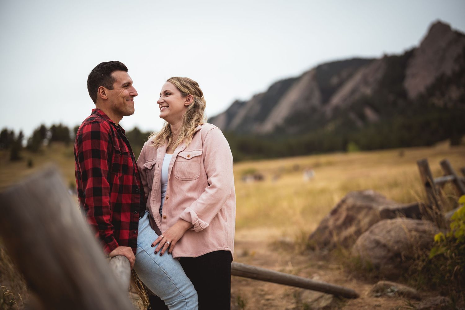 A couple shares a tender moment on a mountain cliff with dramatic landscapes in the background.