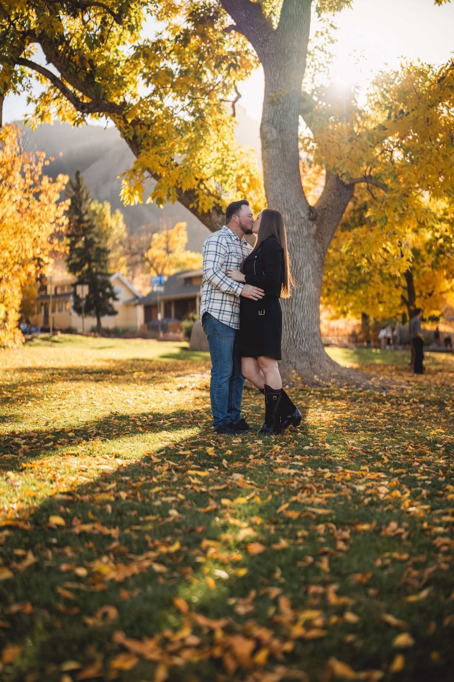 A couple sharing an intimate moment under a golden autumn tree with sunlight streaming through.