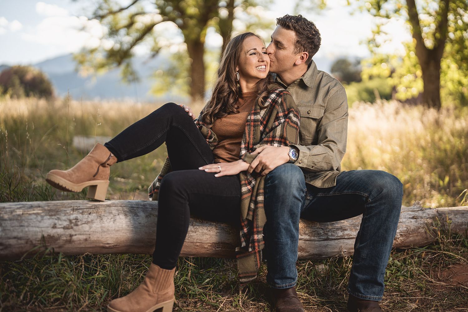 Romantic couple sits together outdoors in a golden field during sunset while embracing.