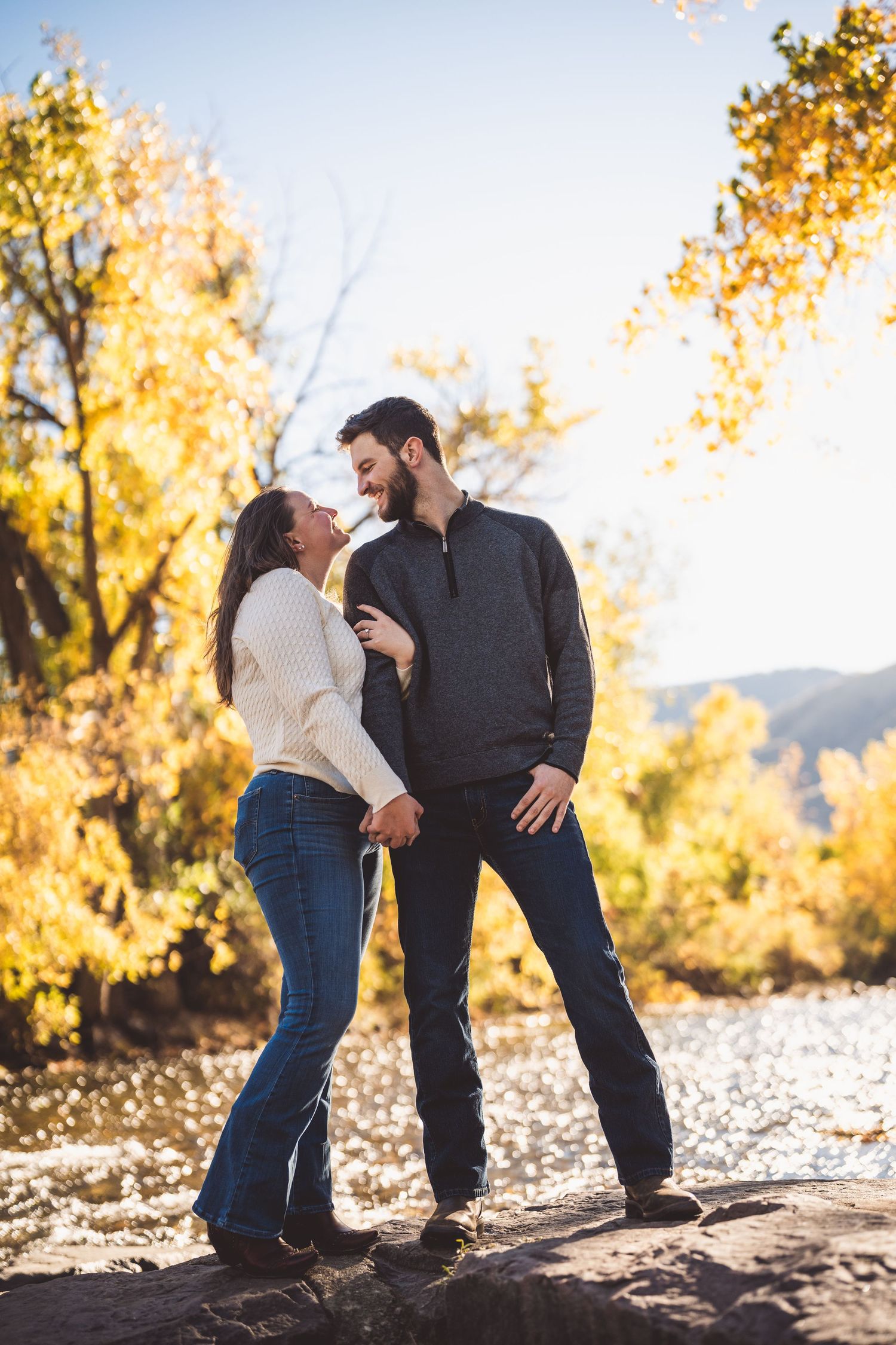 A playful couple interacting on rocky terrain surrounded by fall foliage.