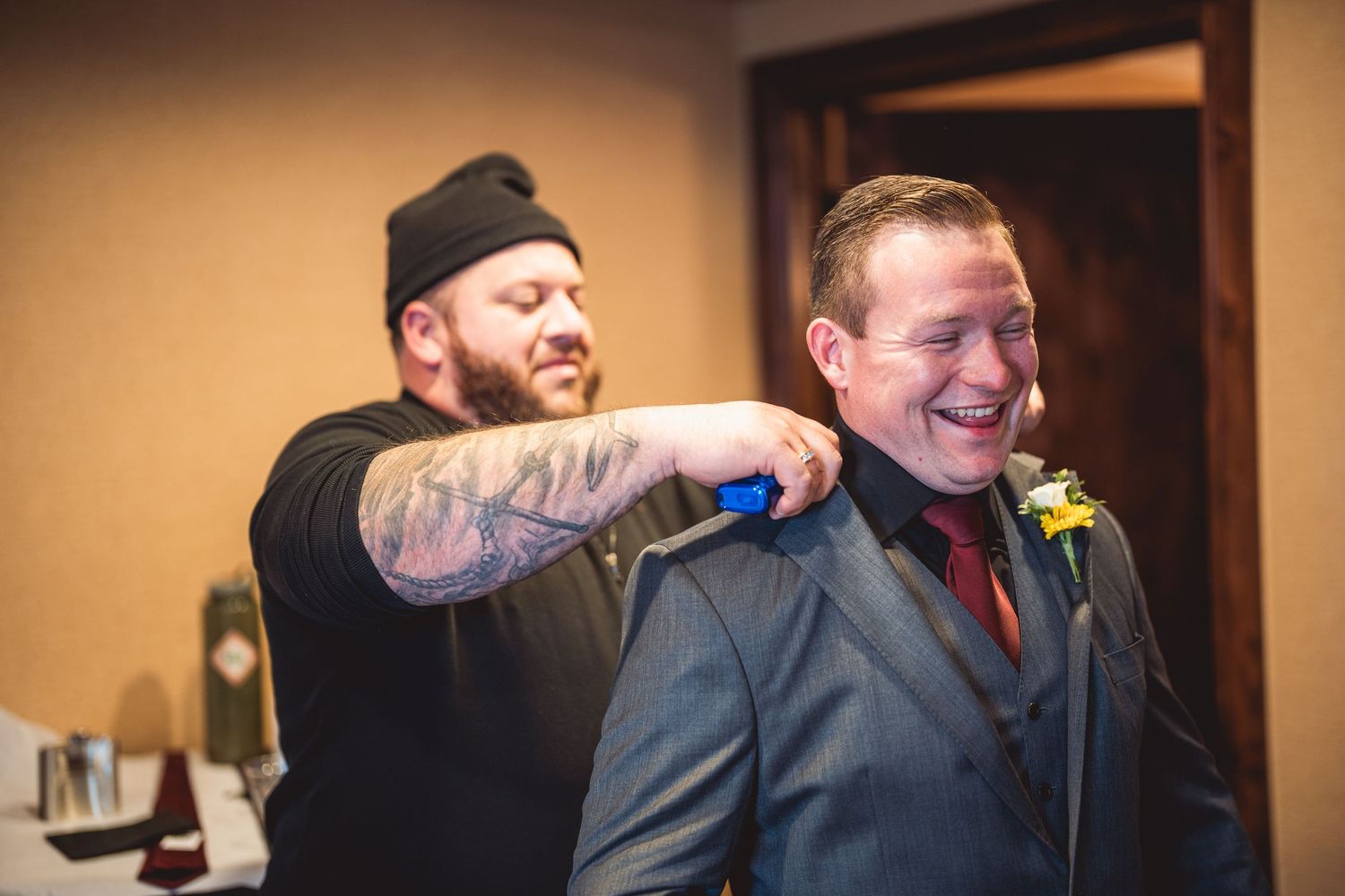 A person helps adjust formal attire during wedding preparation in an indoor setting.