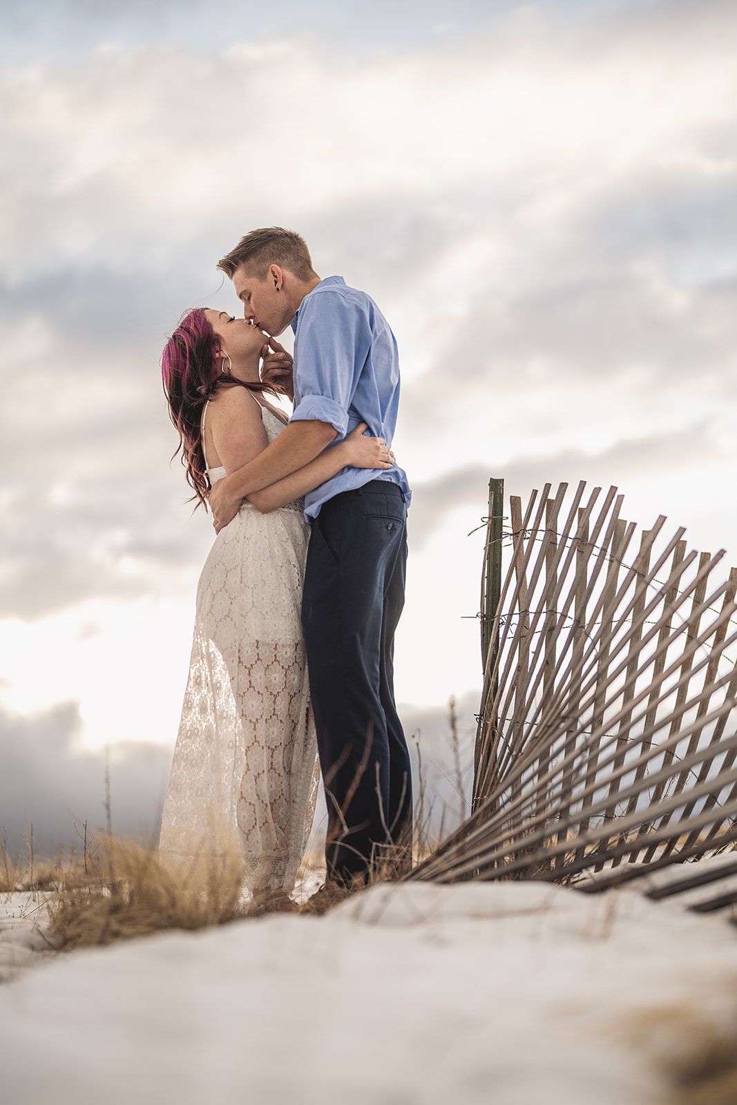Romantic moment captured near wooden fence at dusk with cloudy skies.