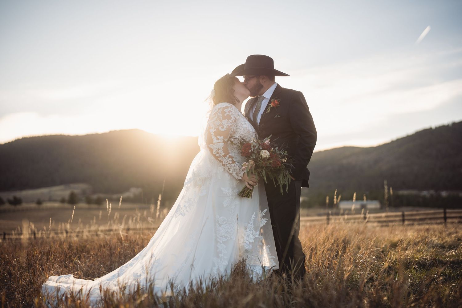 Romantic silhouettes of newlyweds dancing in golden sunset light with mountains in background.