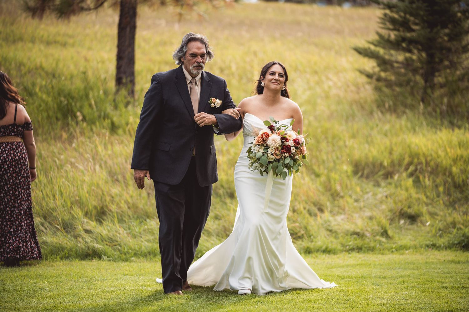 Wedding party gathers on grassy hillside for outdoor ceremony photos.