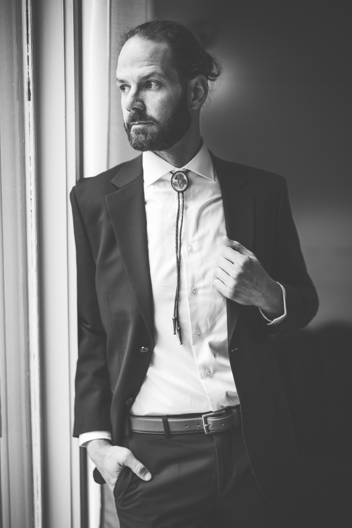Black and white photos of a groom in formal attire by a window.