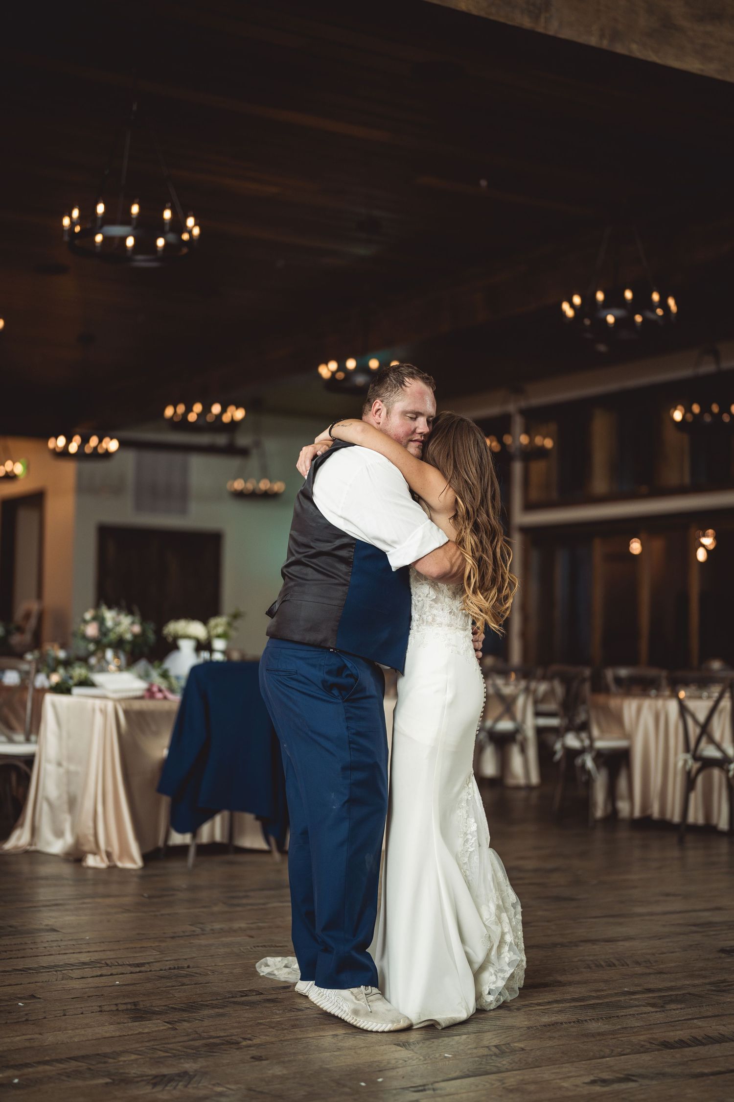 Bride and groom share their first dance in an elegantly decorated wedding reception hall with warm chandelier lighting.