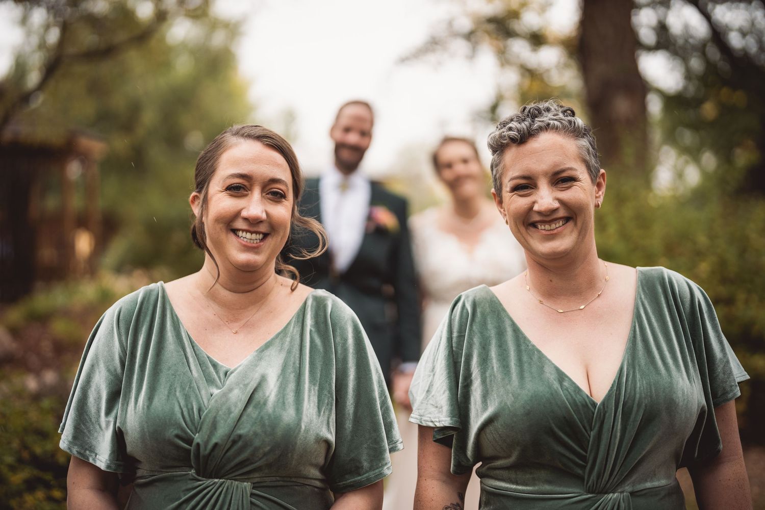 Bridesmaids wearing matching sage green dresses stand together during an outdoor wedding.