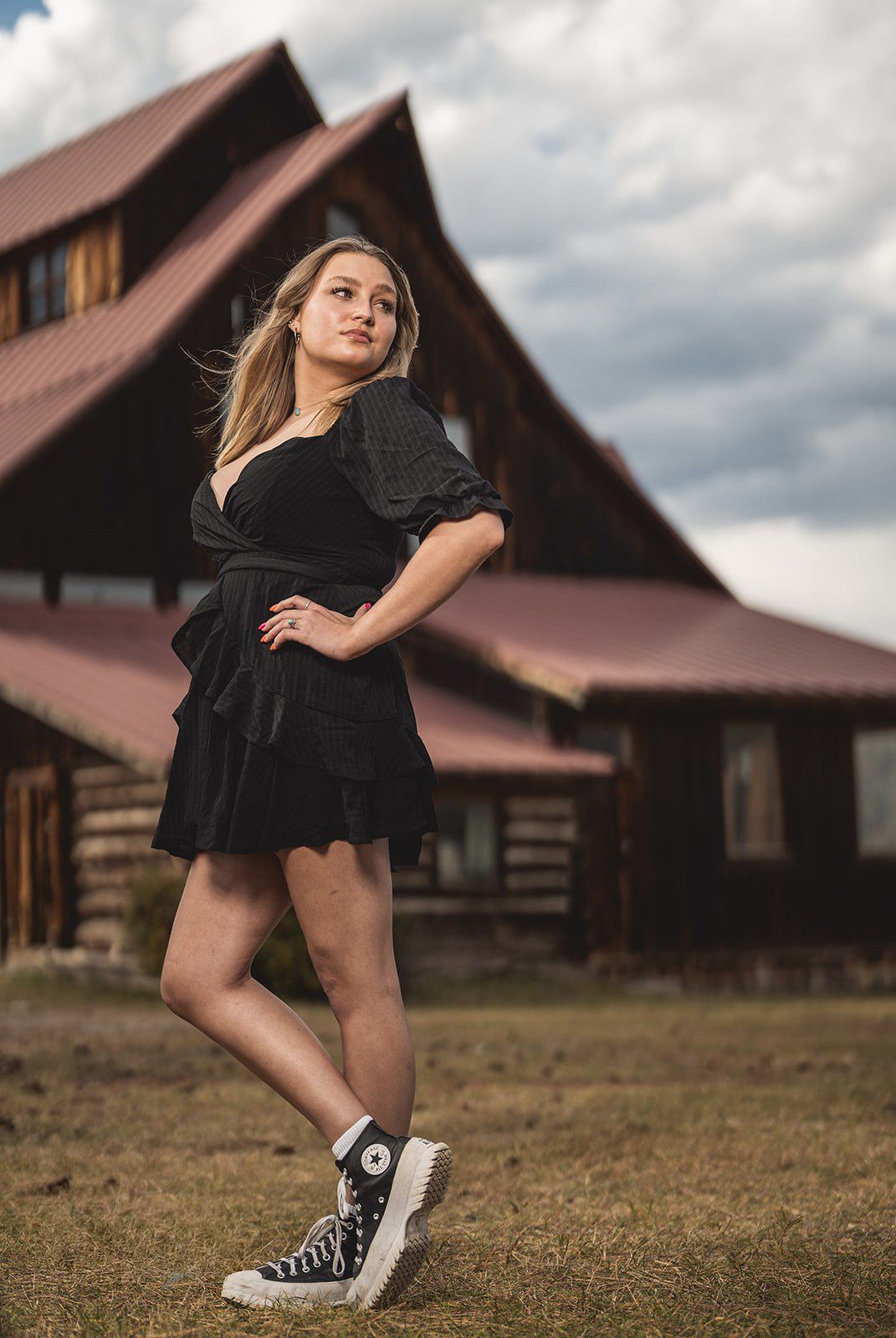 Dance-inspired portrait in black dress with rustic barn buildings in background.