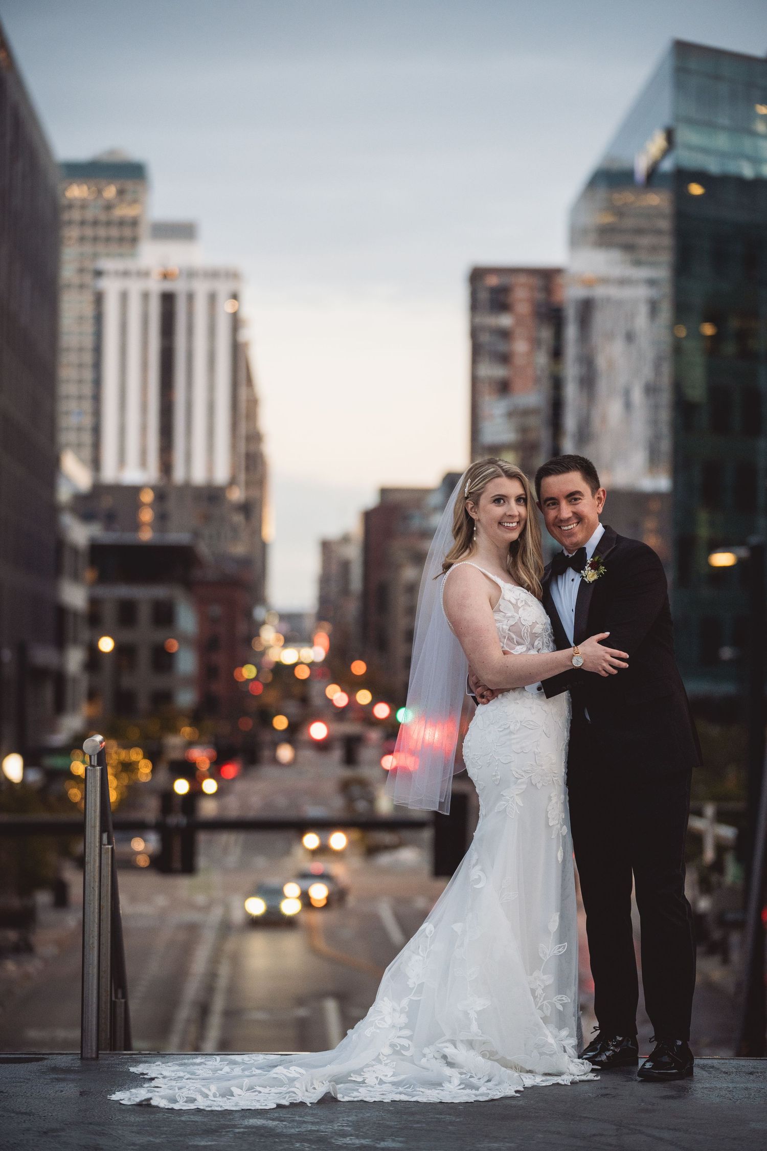 Elegant couple poses against urban cityscape during golden hour.