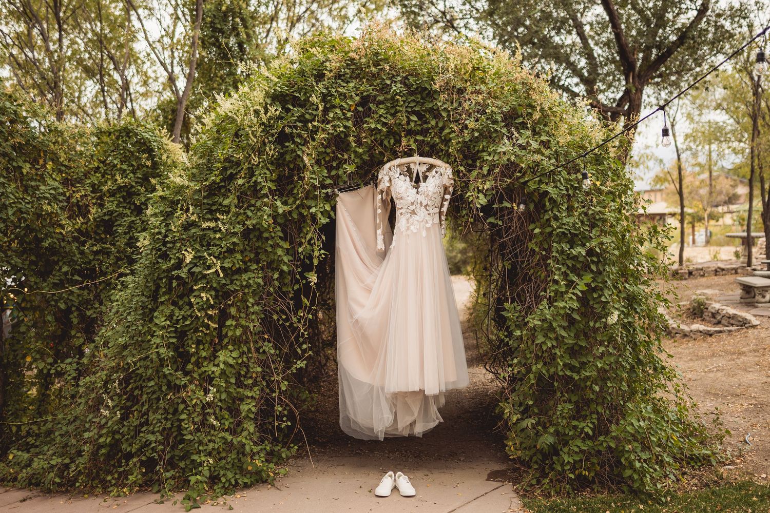Wedding dress displayed in a garden archway surrounded by green foliage.