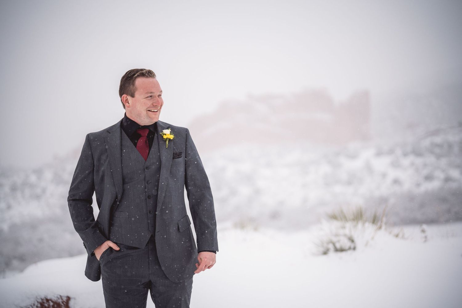 Winter wedding portraits of groom in charcoal suit against snowy mountain backdrop.