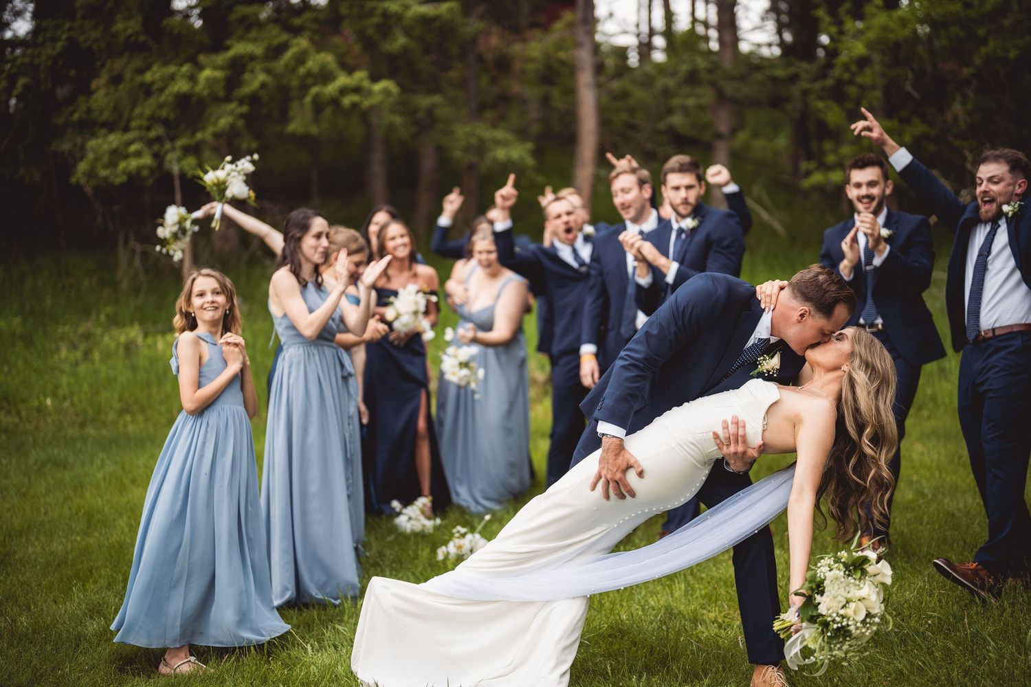 Celebratory moment at an outdoor wedding with bridal party in blue and navy attire.