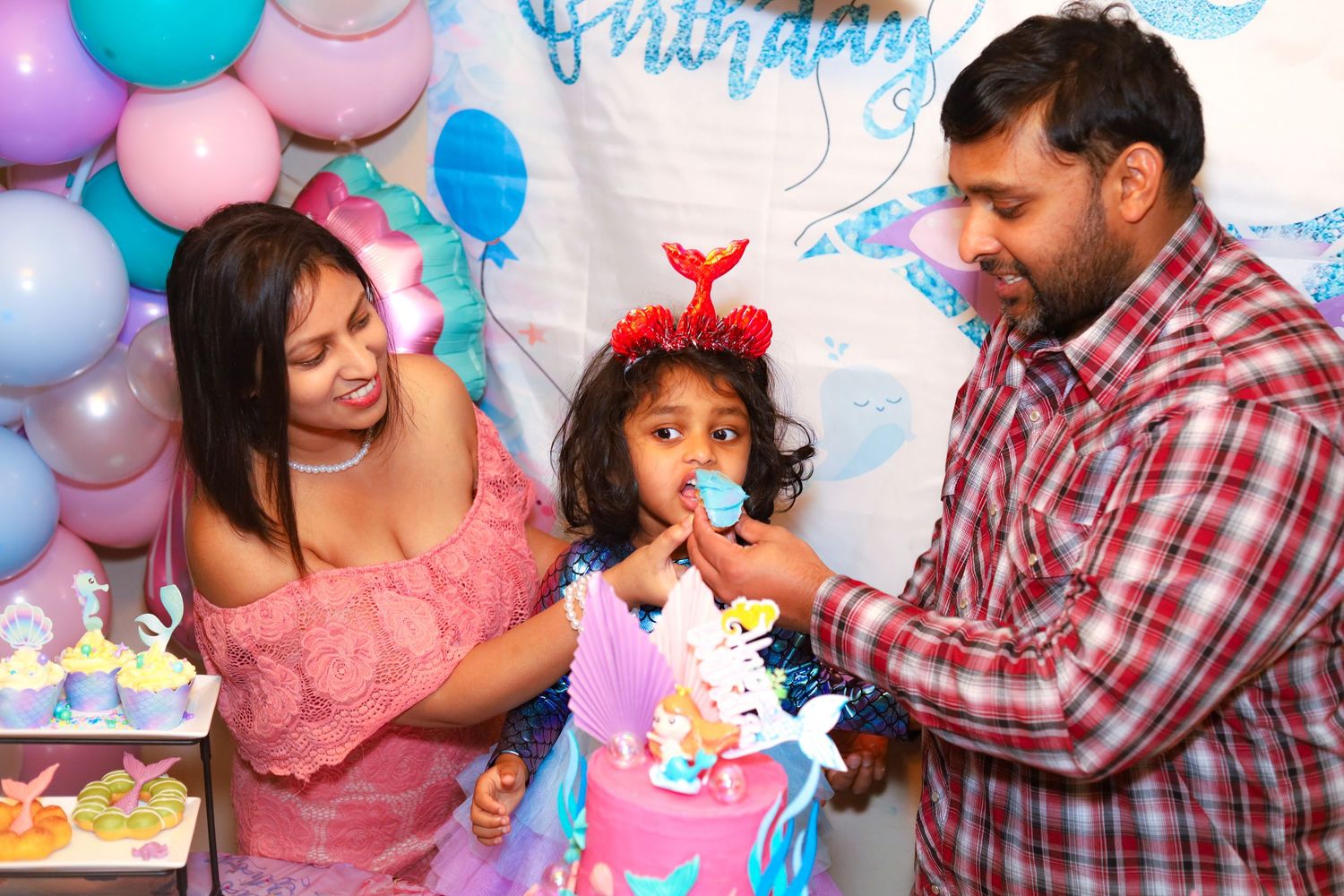 Two parents feeding the birthday girl a piece of birthday cake.