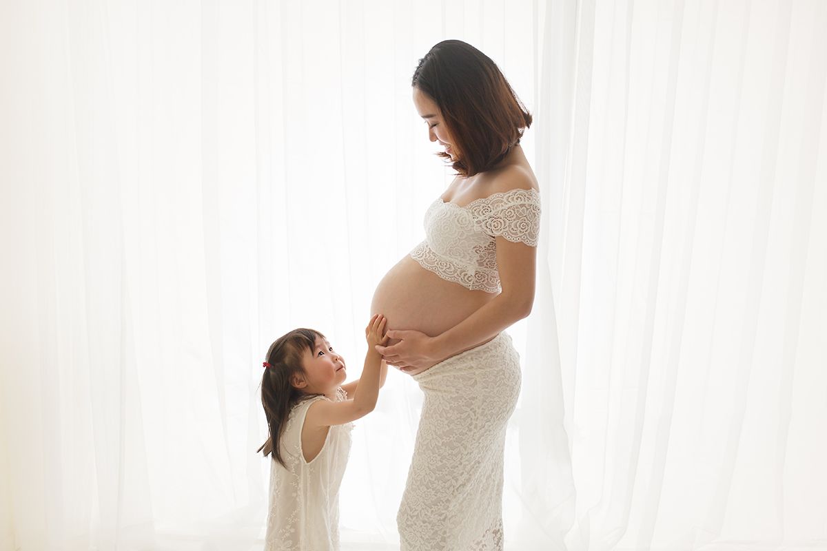 Mother and child bonding photos in white against bright window.