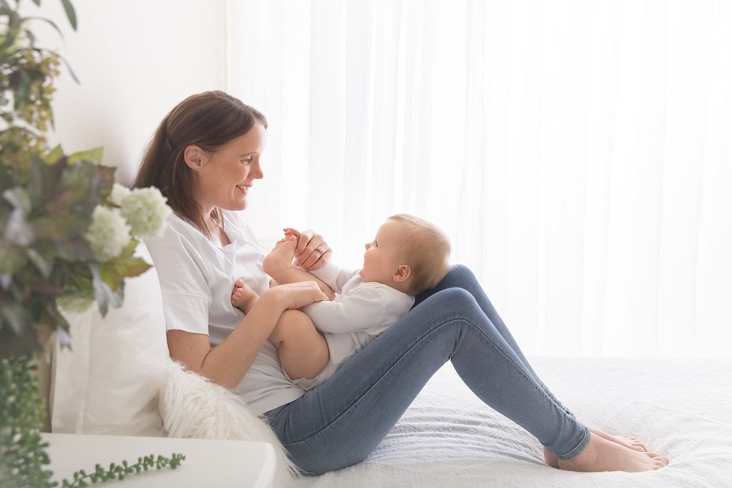 Family portrait on white bed with floral decorations and natural window light.