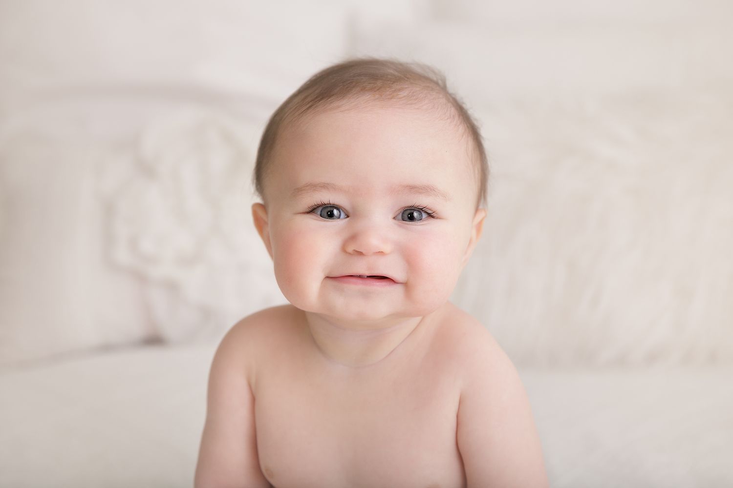 Baby smiling during professional milestone photo session on white background.