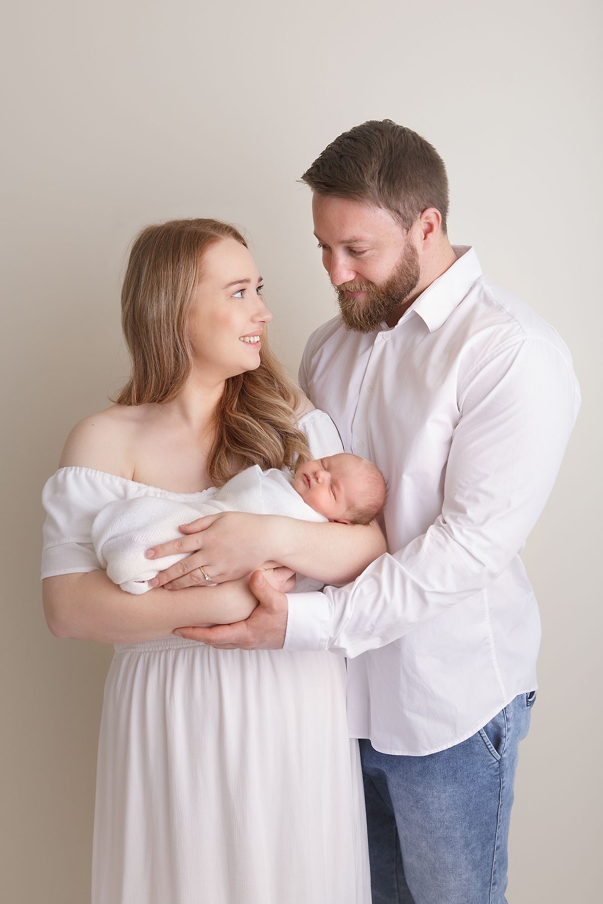 Family newborn photography with parents in white and denim against neutral backdrop.