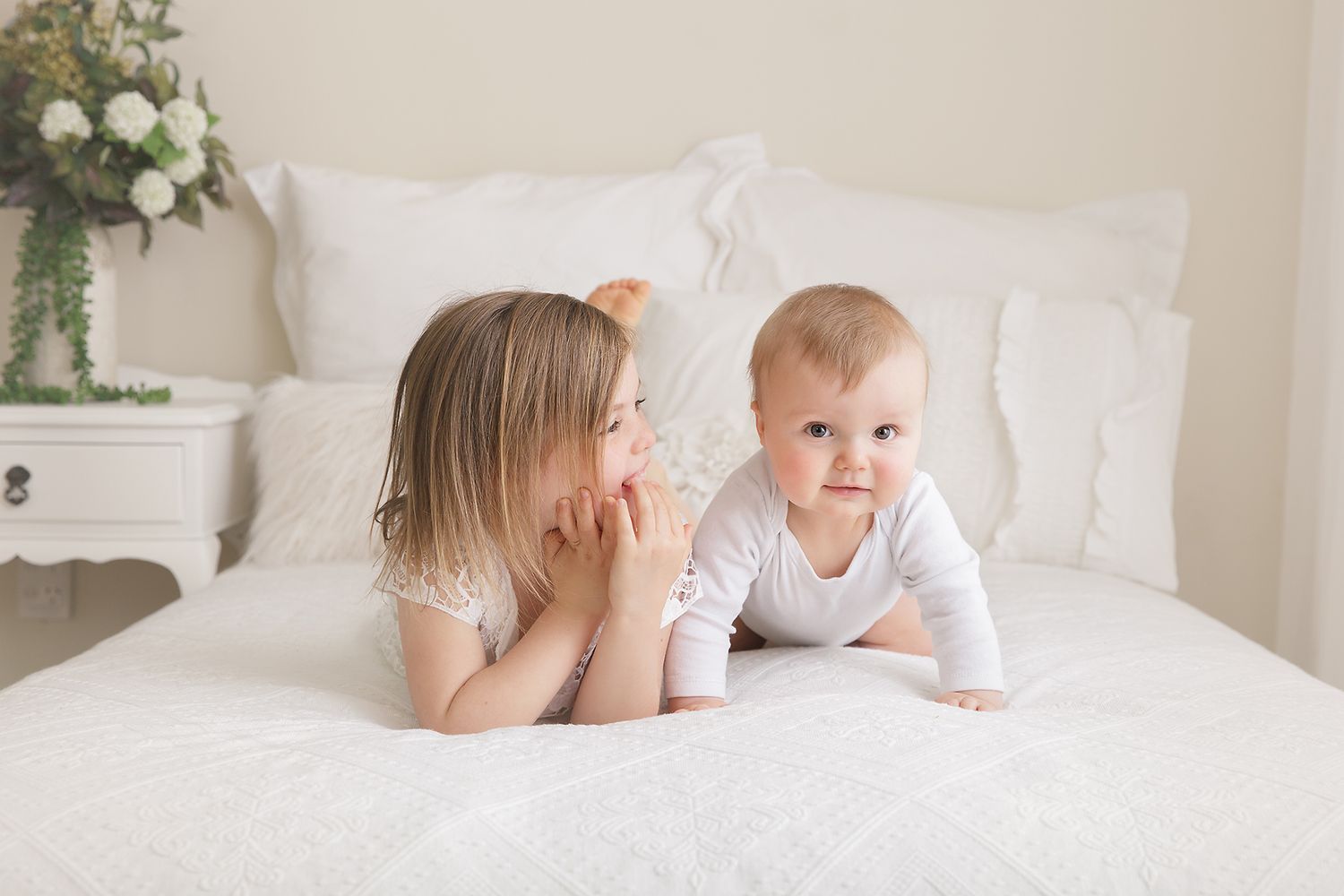 Intimate family photography session on white bed with decorative greenery.
