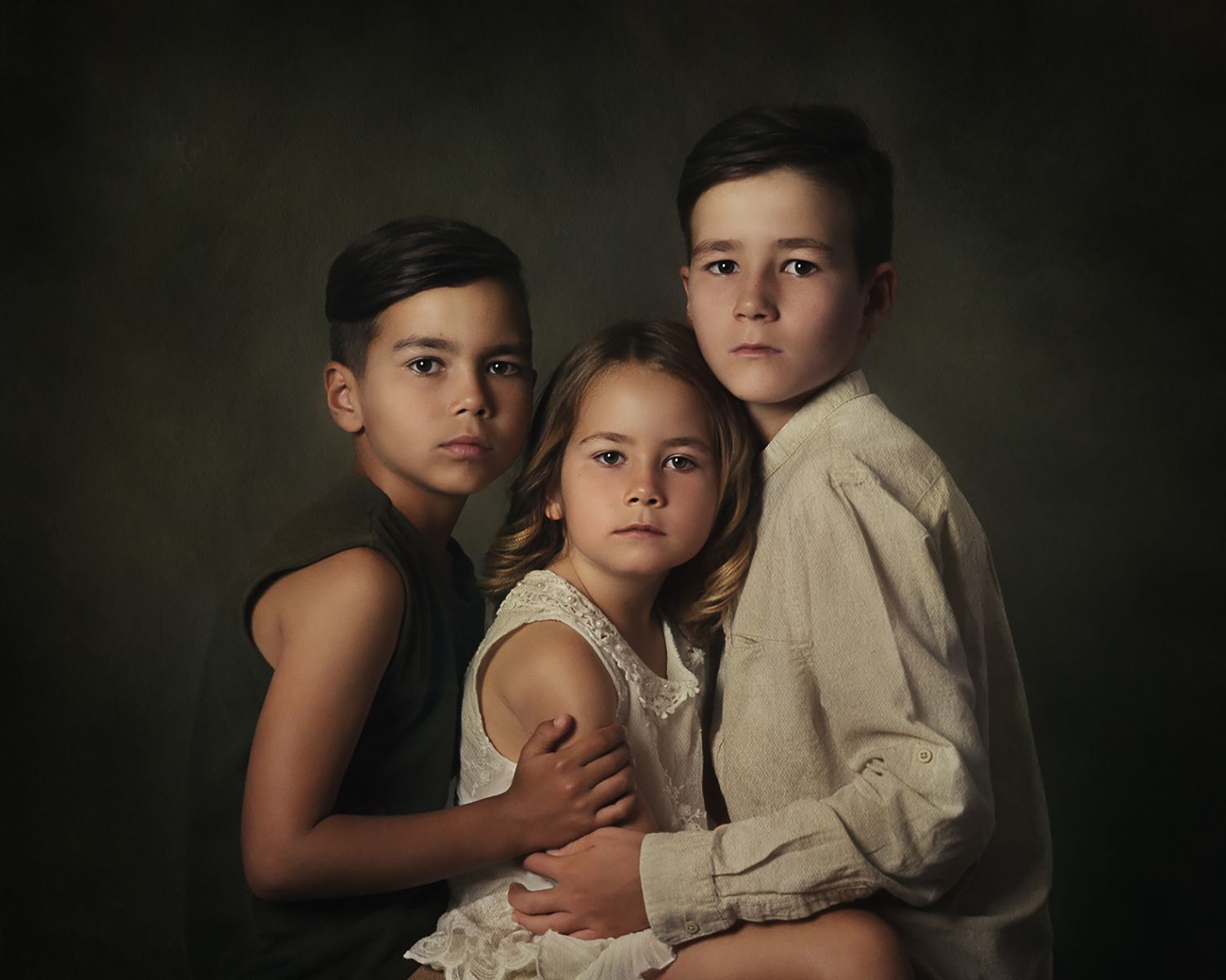 Fine art portrait of three siblings in dramatic lighting against dark background.