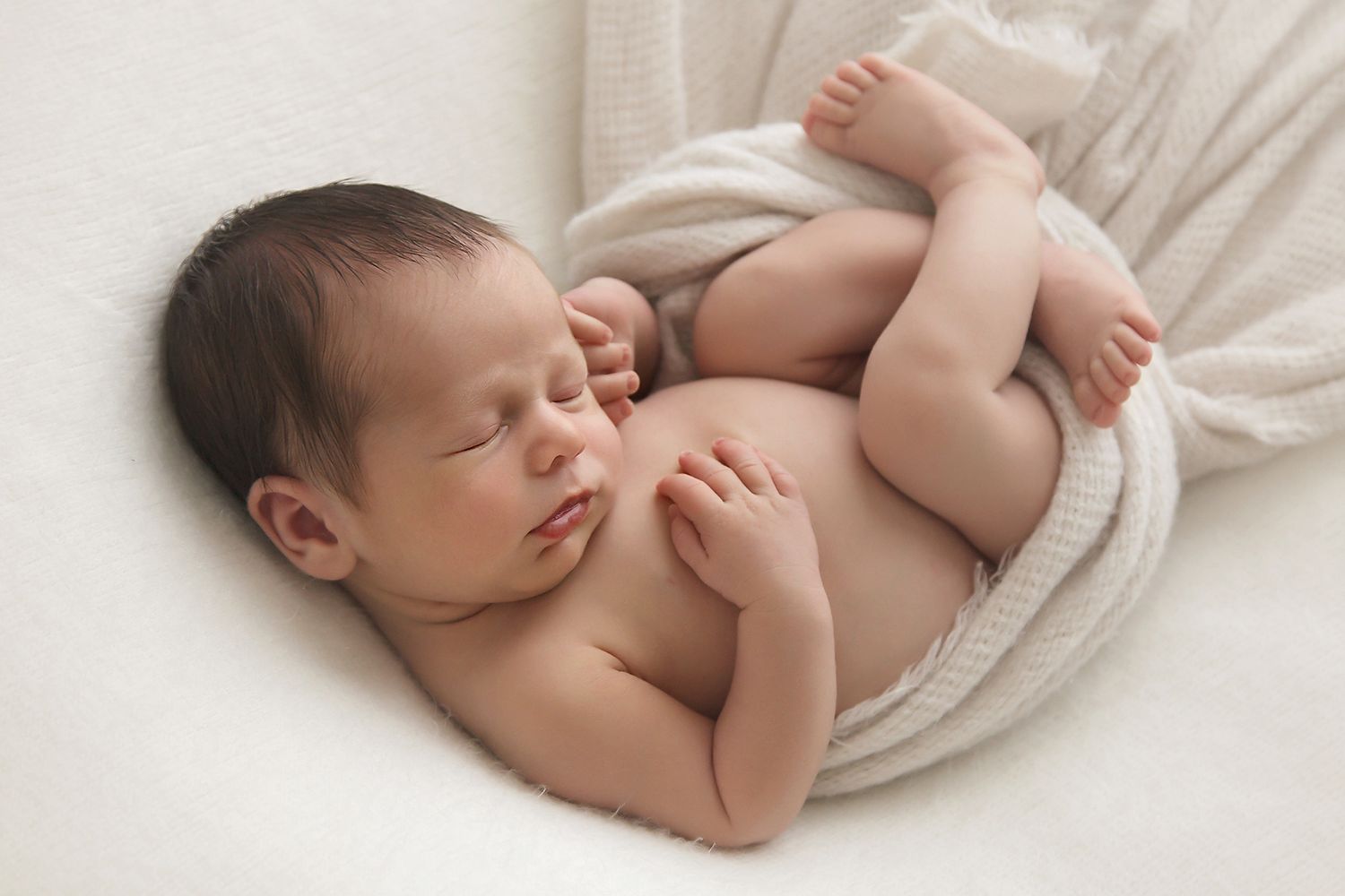 Peaceful sleeping newborn wrapped in soft white fabric on light background.