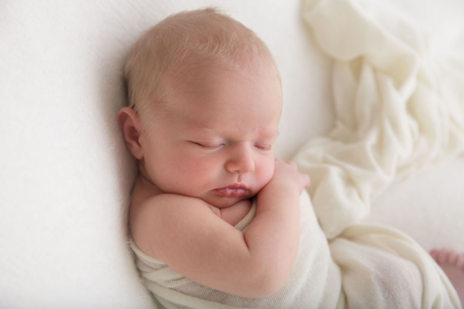 Sweet newborn baby resting on cream colored fabric during professional photoshoot.