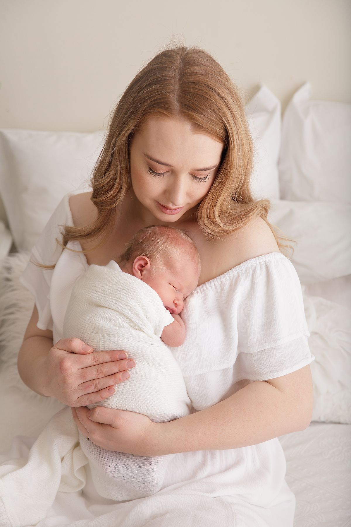 Tender newborn photography session with mother in white.
