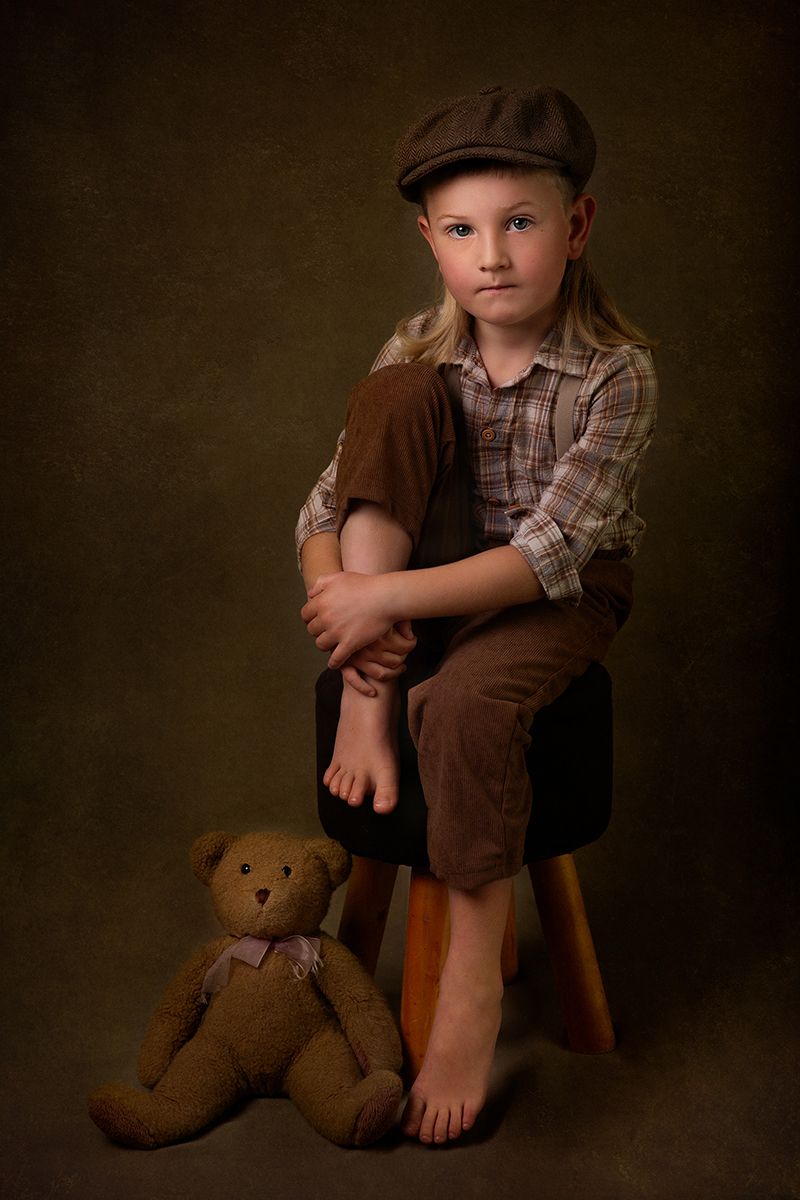 Vintage-inspired portrait with brown tones showing a teddy bear companion and newsboy cap.