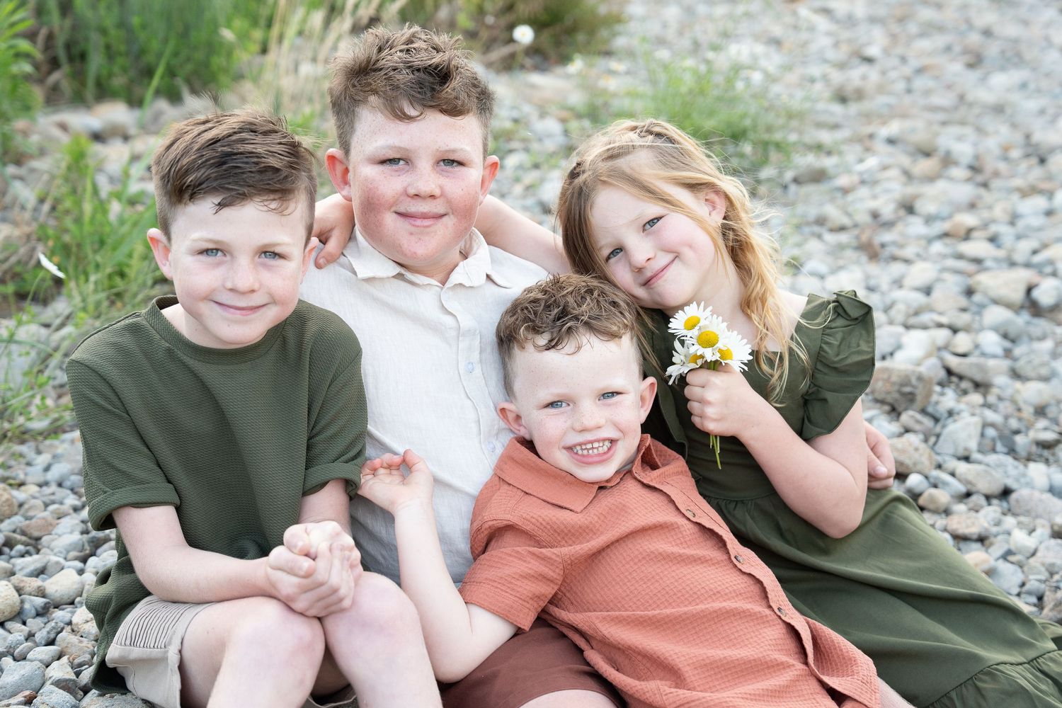 A group sits together on a rocky beach shore while smiling and laughing during a casual outdoor photo session.