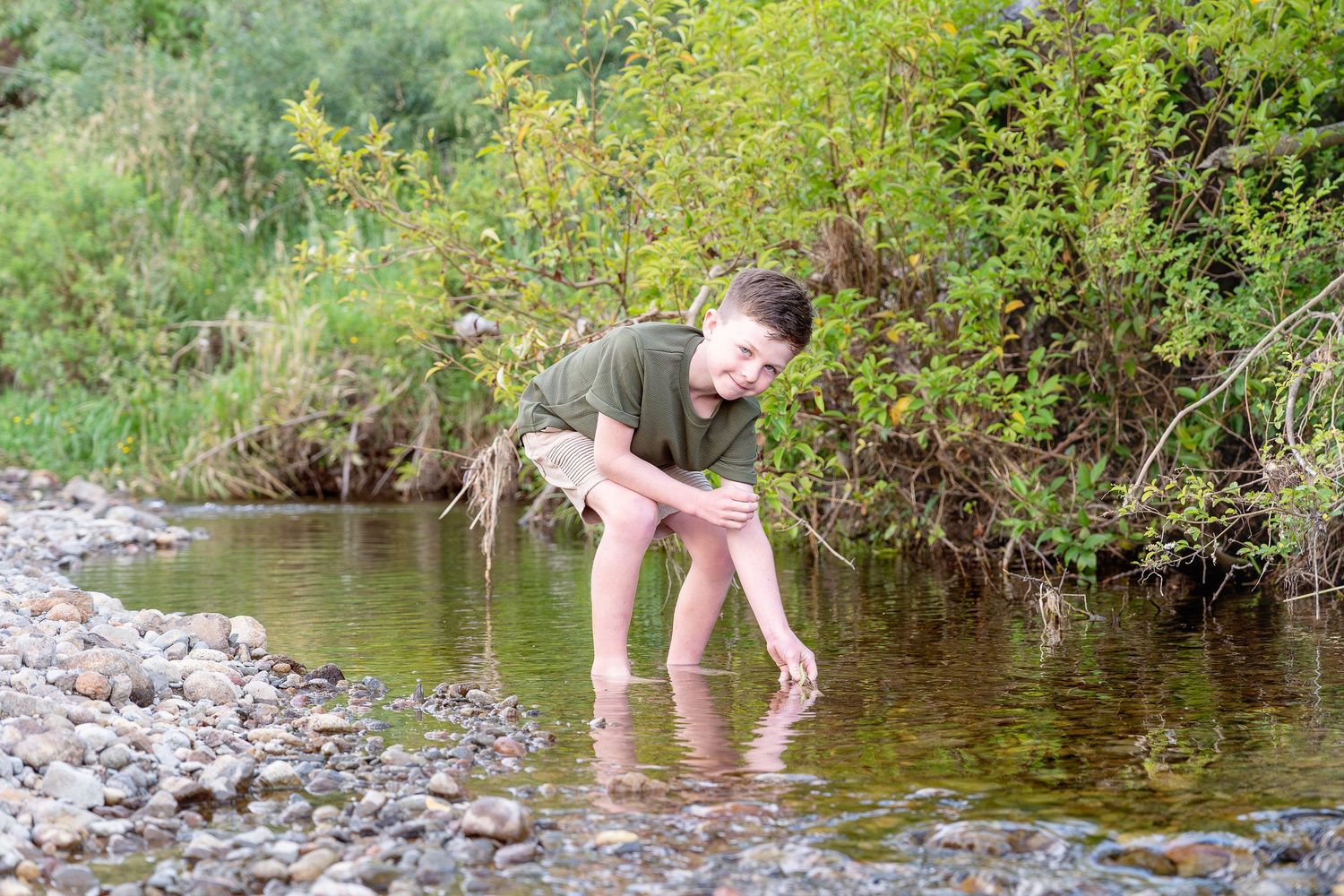 A person wades through a shallow stream while exploring nature on a sunny summer day.